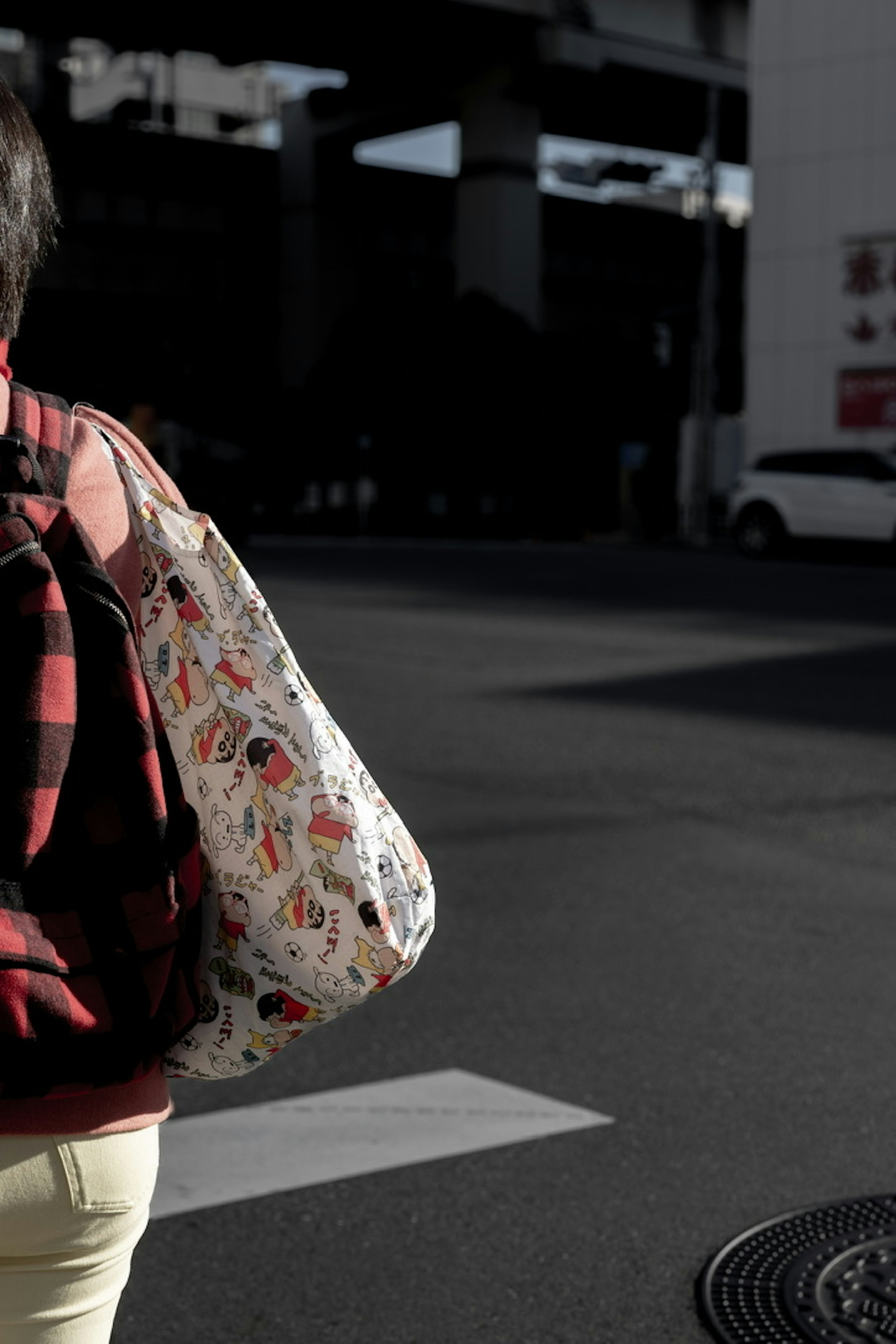 A person wearing a red and black checkered backpack crossing a crosswalk