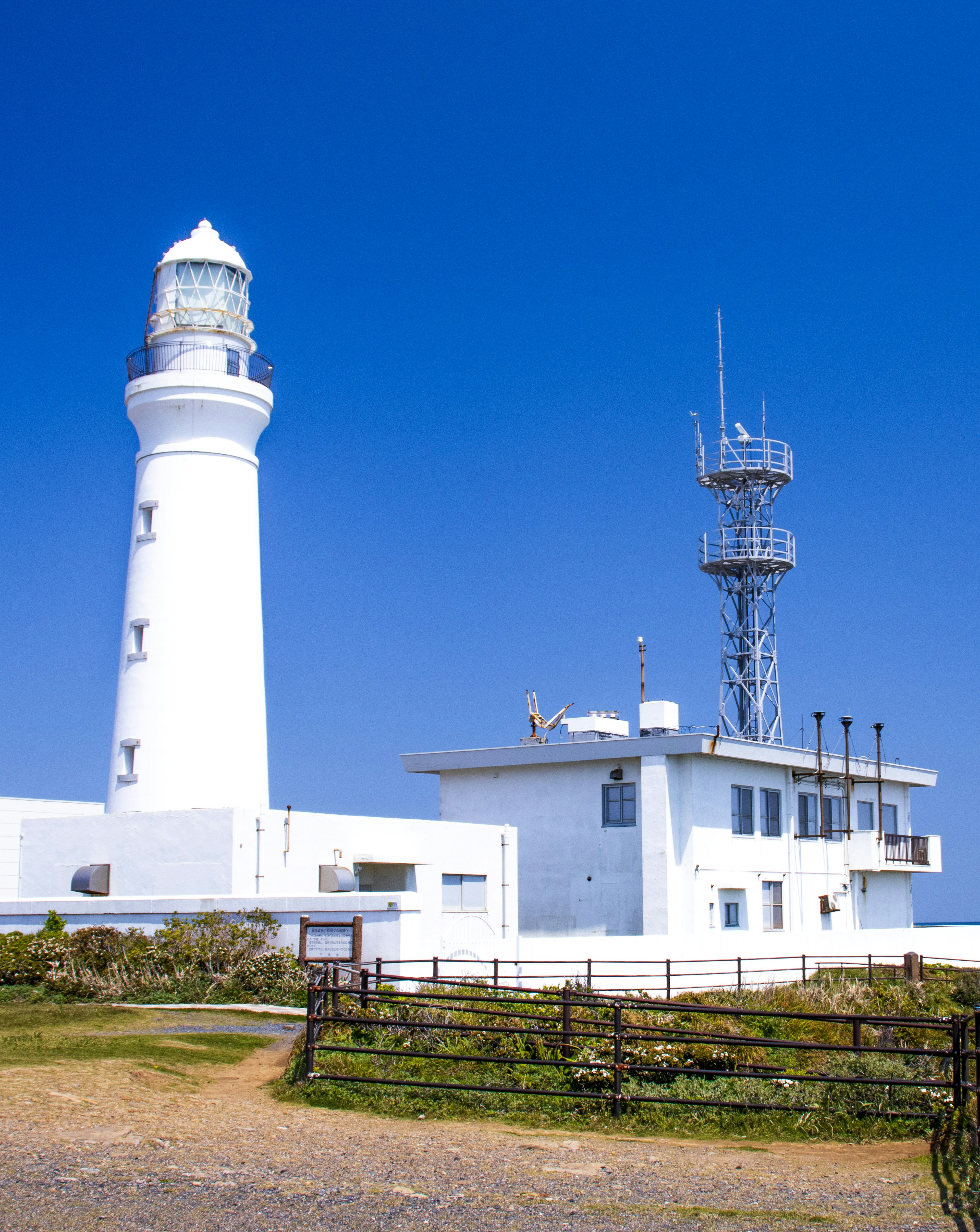 A white lighthouse and communication tower under a blue sky