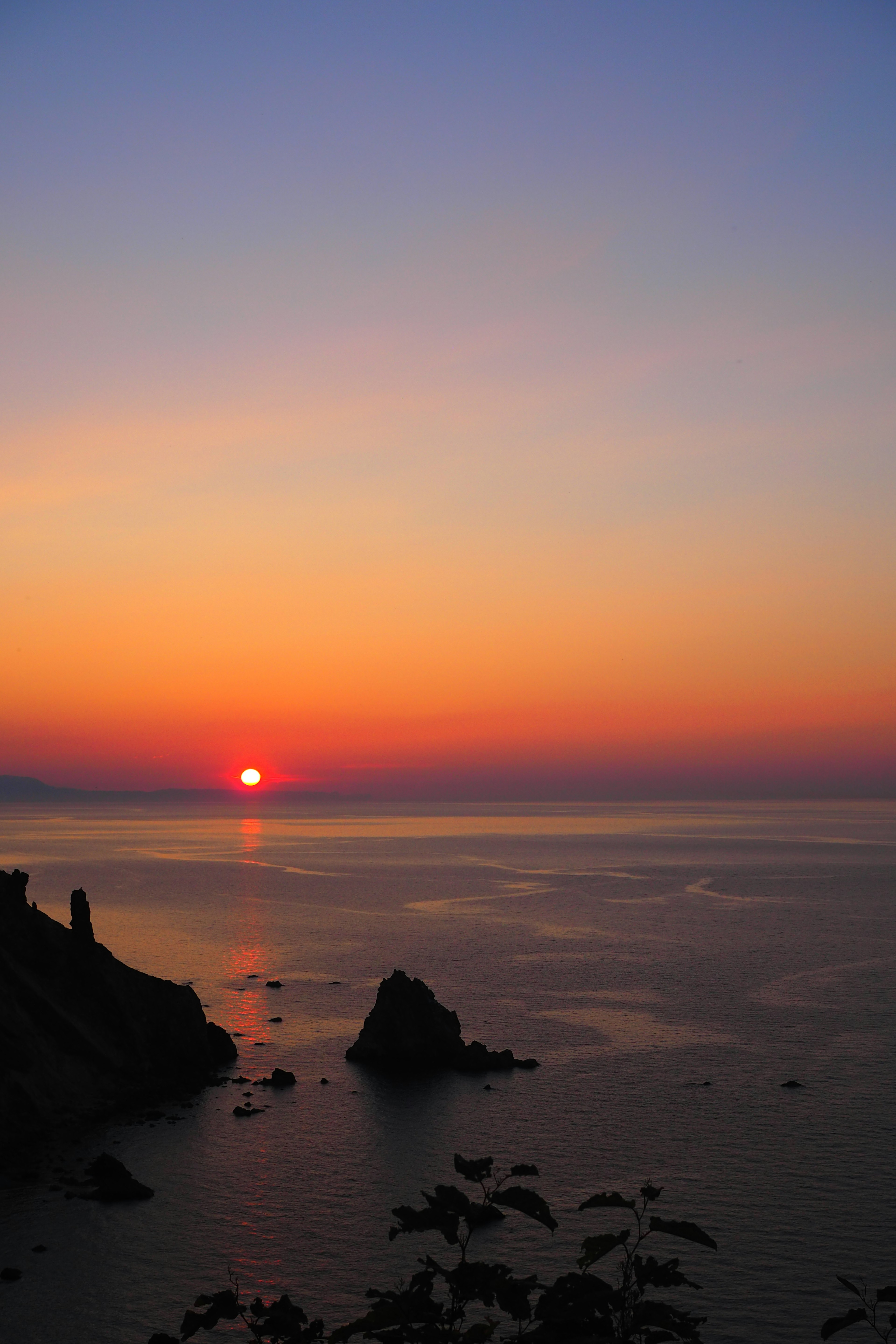 美麗的海景，夕陽在平靜的水面和岩石海岸上落下