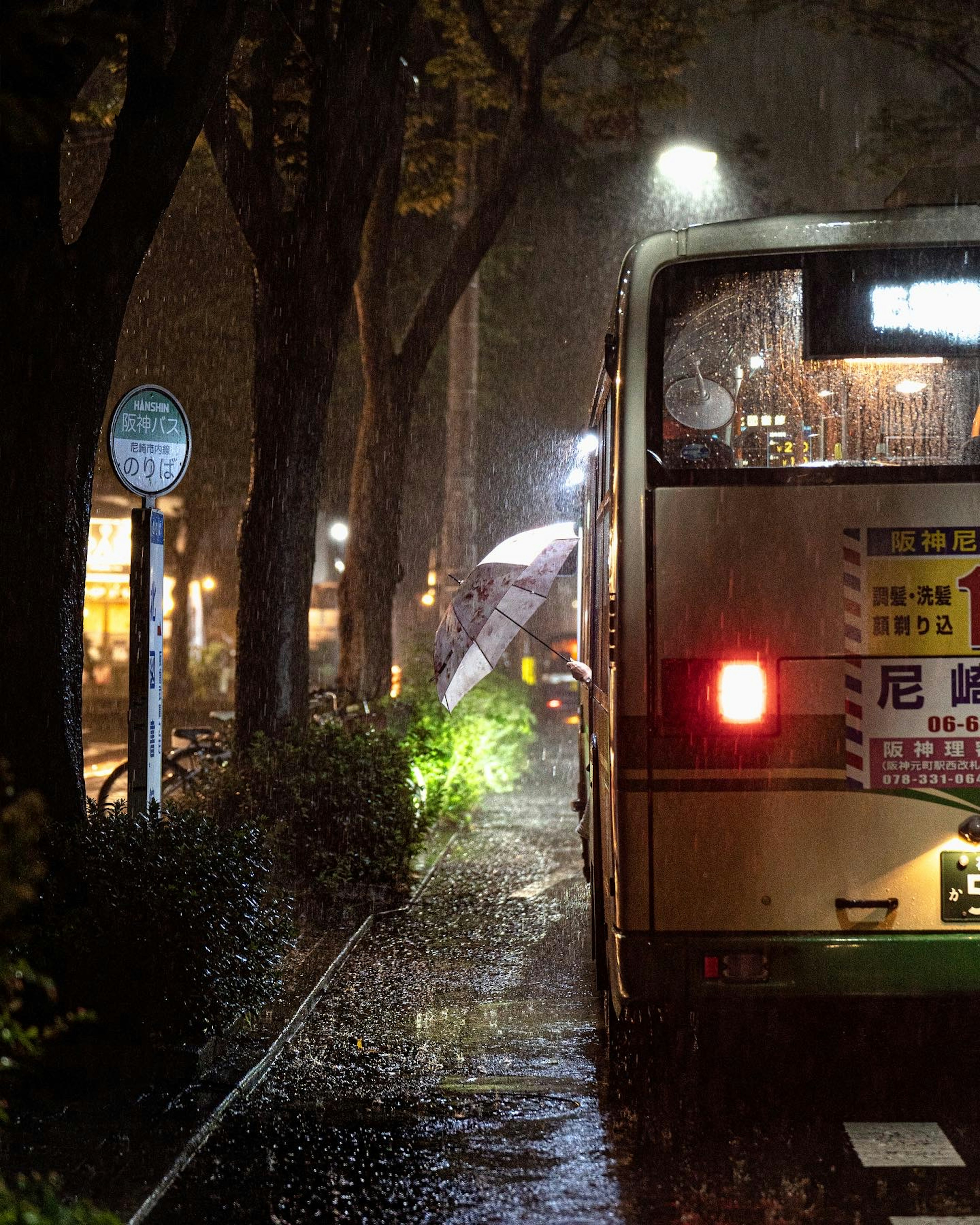 雨の中に停まっているバスと傘をさした人