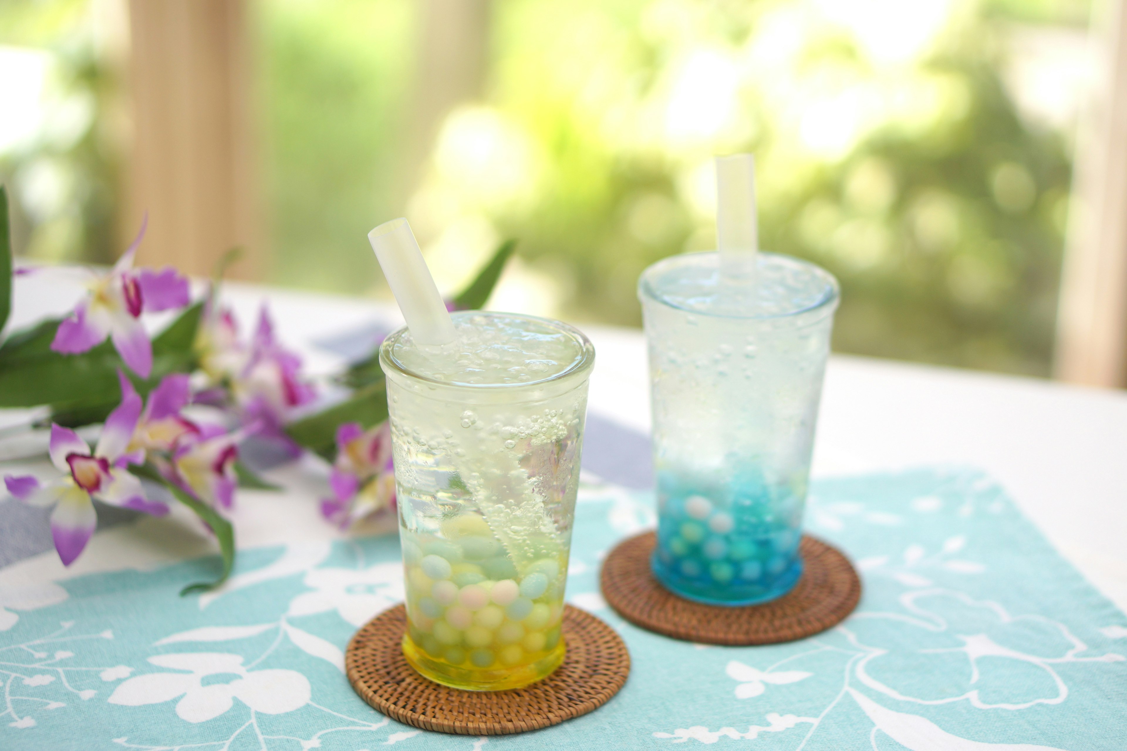 Two glasses with blue and green drinks on a table with beautiful flowers