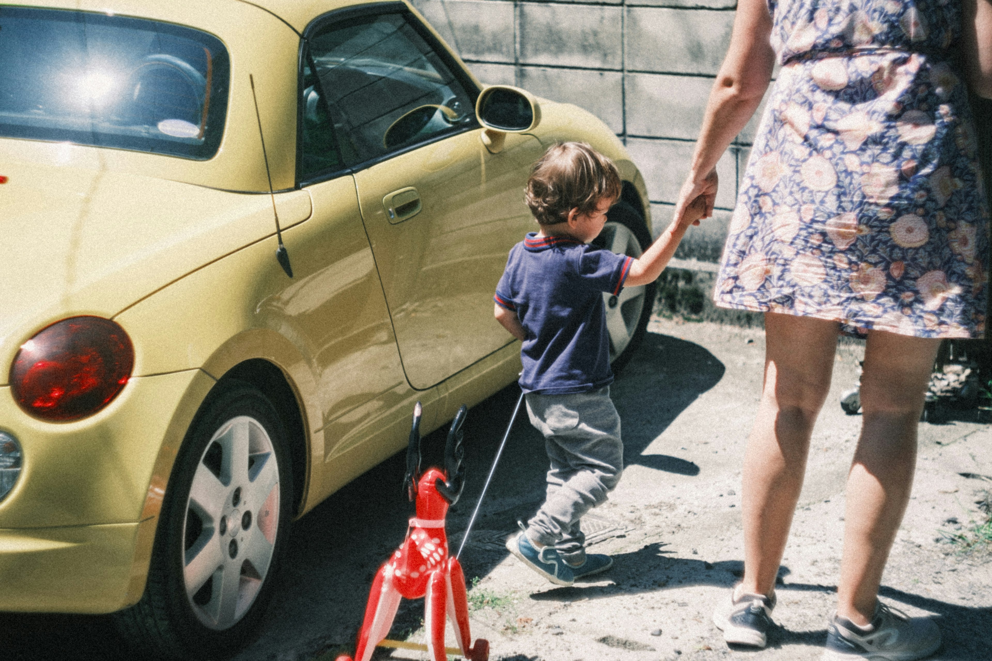 Un niño sosteniendo una correa de perro caminando junto a un coche amarillo