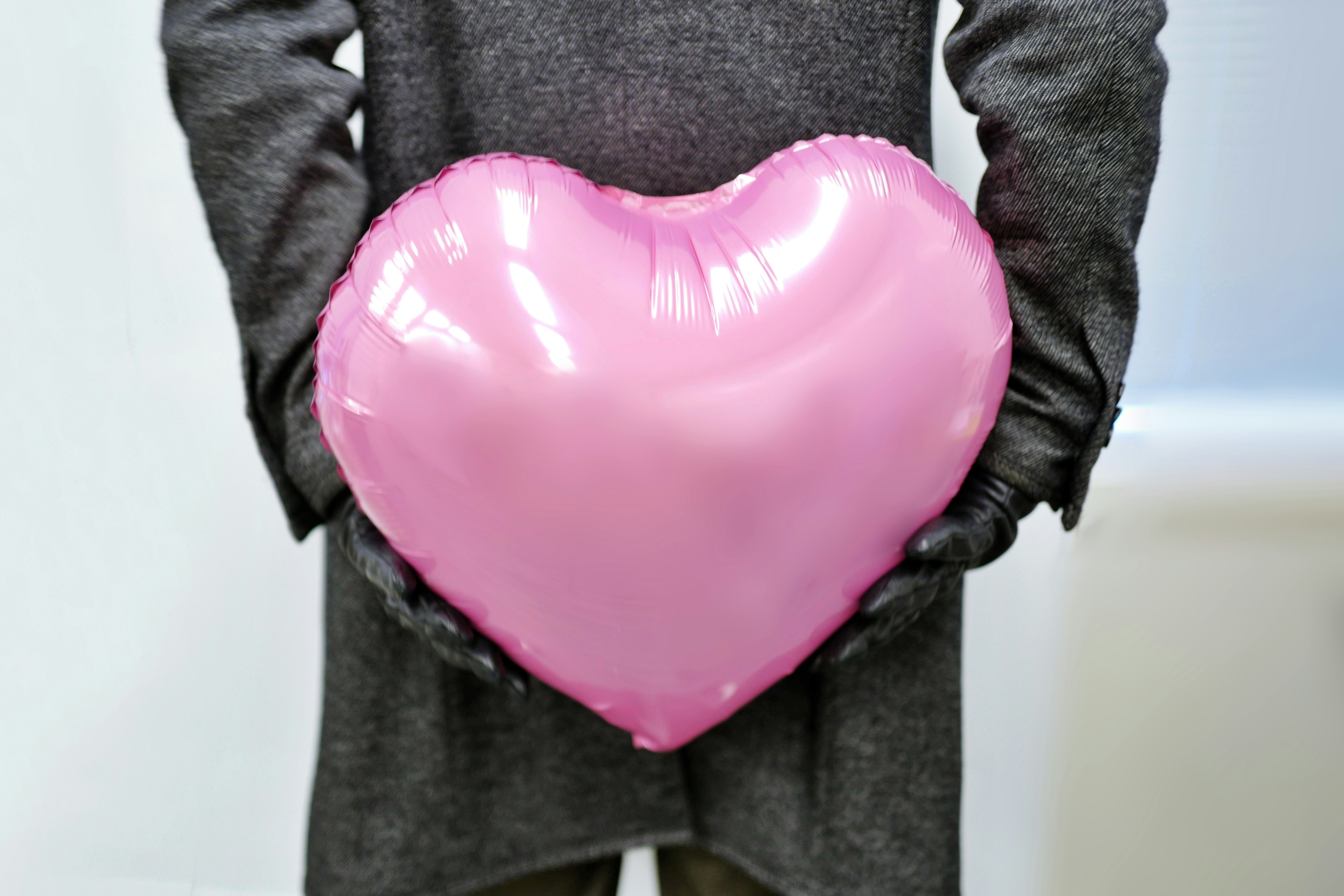 A person holding a pink heart-shaped balloon behind their back