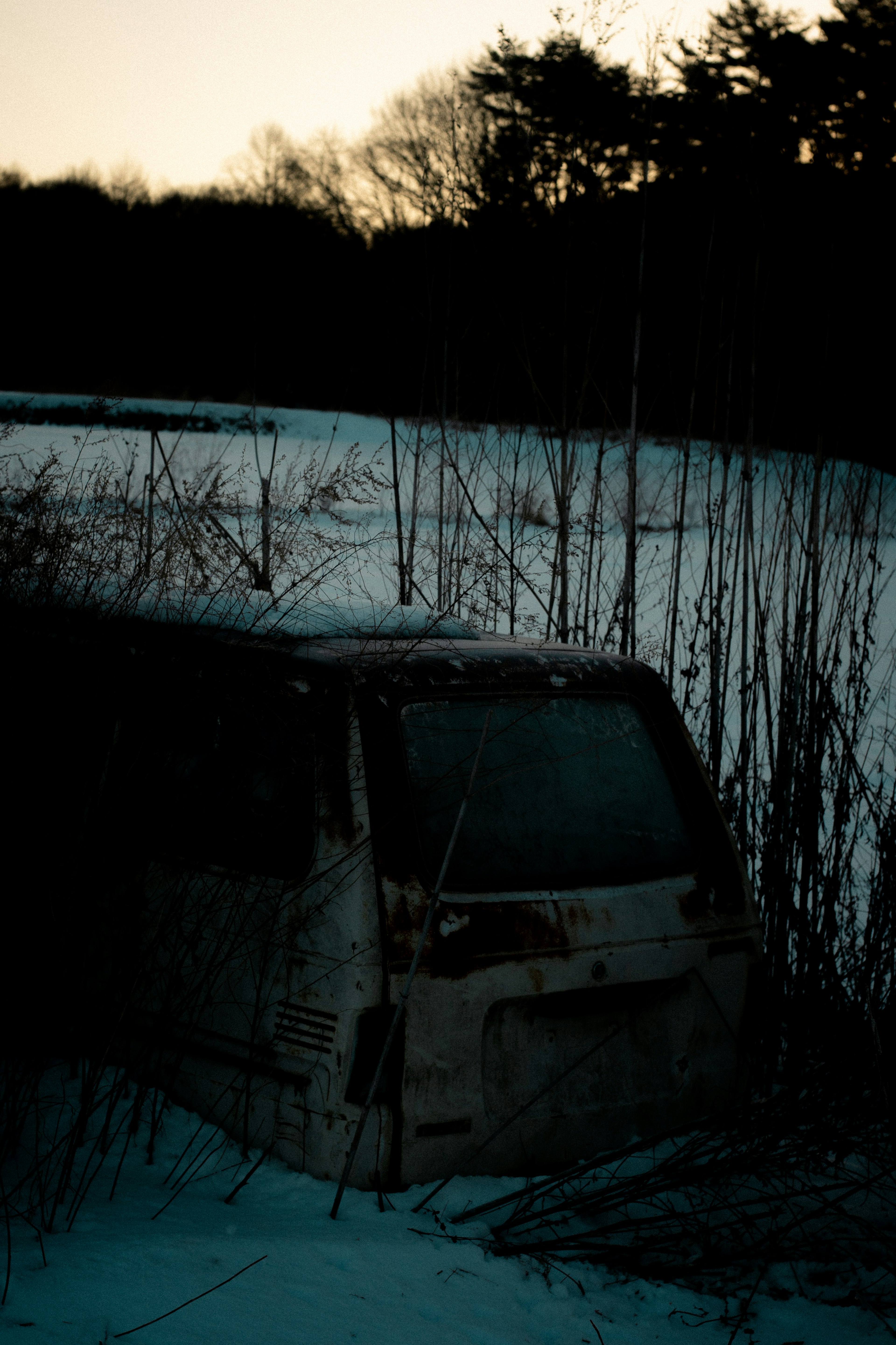 Abandoned vehicle partially buried in snow with a sunset backdrop