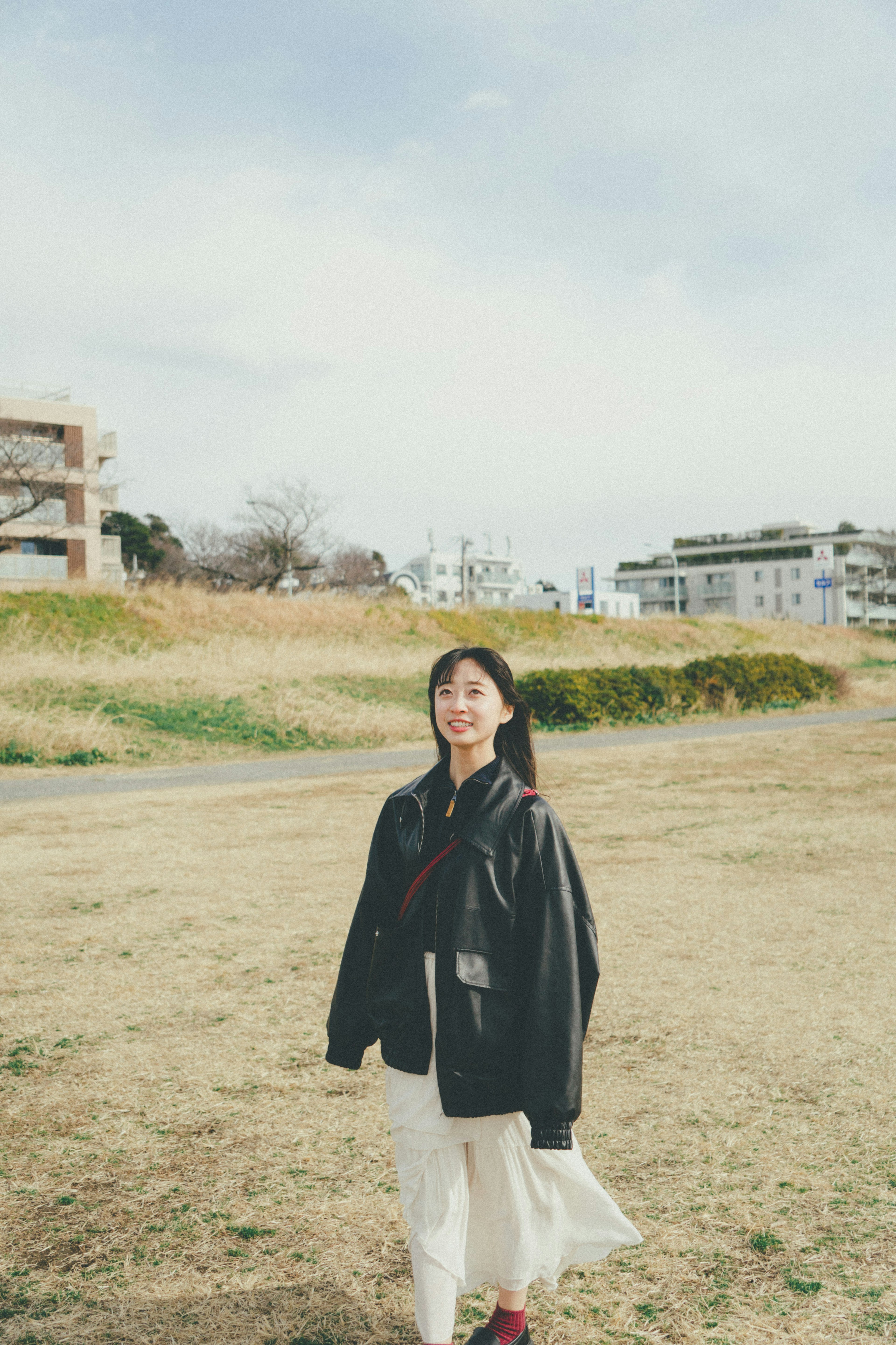 Woman in a black jacket and white skirt smiling in a grassy field