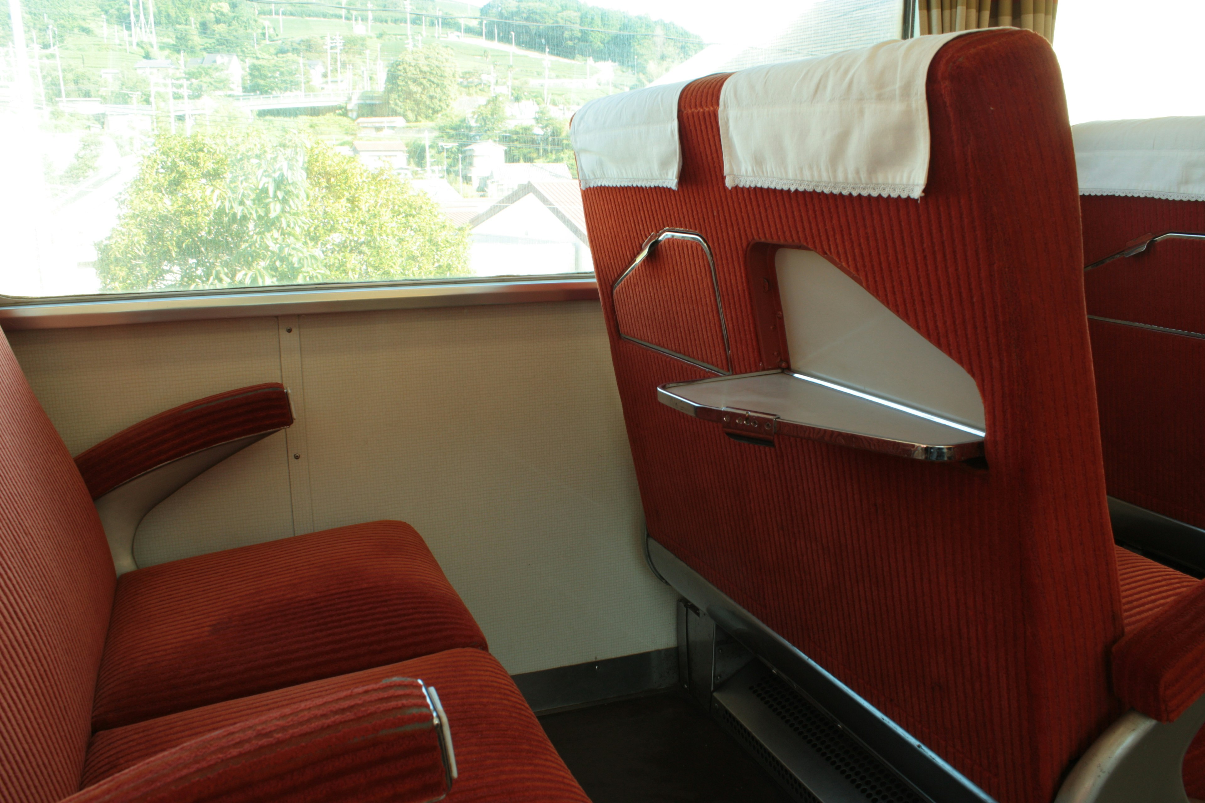 Vista interna di un treno con sedili rossi e un paesaggio verde visibile attraverso il finestrino