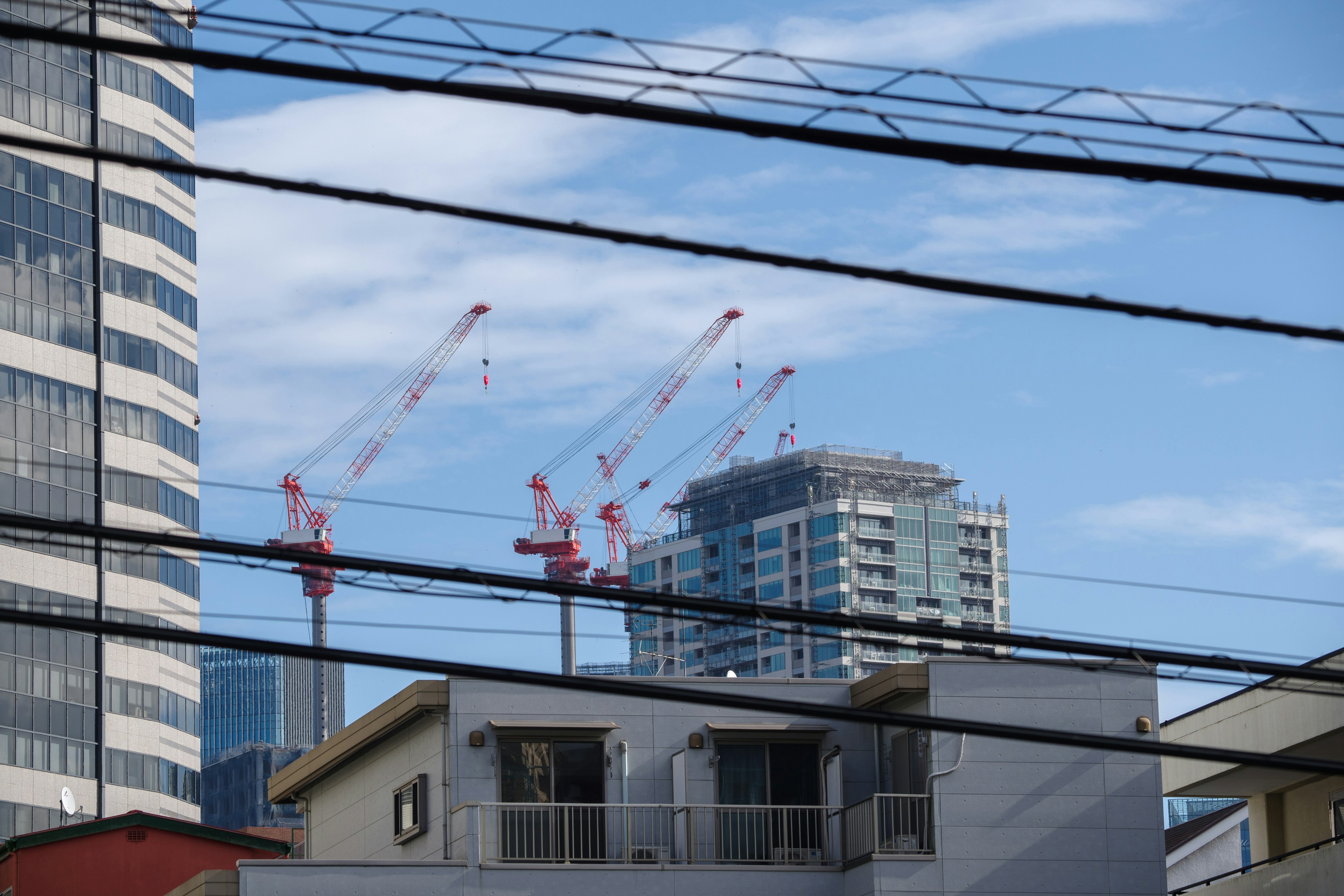 Paisaje urbano con grúas de construcción y un rascacielos bajo un cielo azul