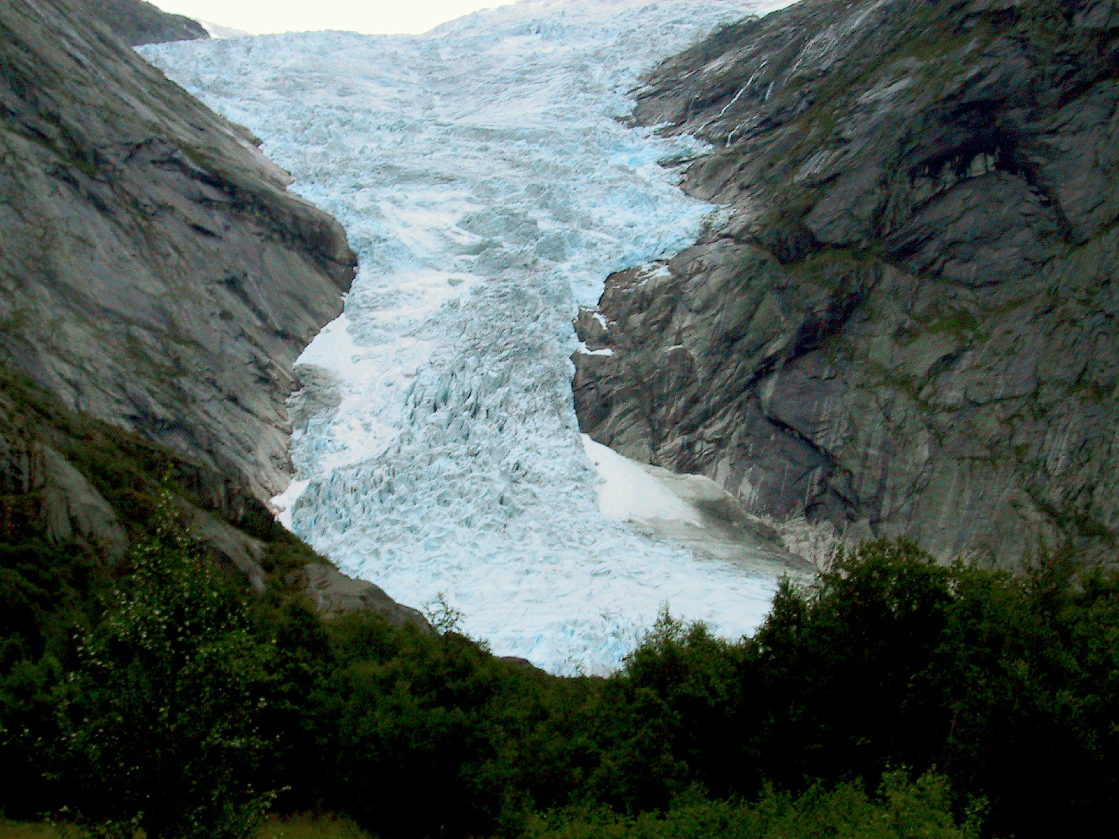 Glacier flowing between mountains surrounded by greenery and rocks