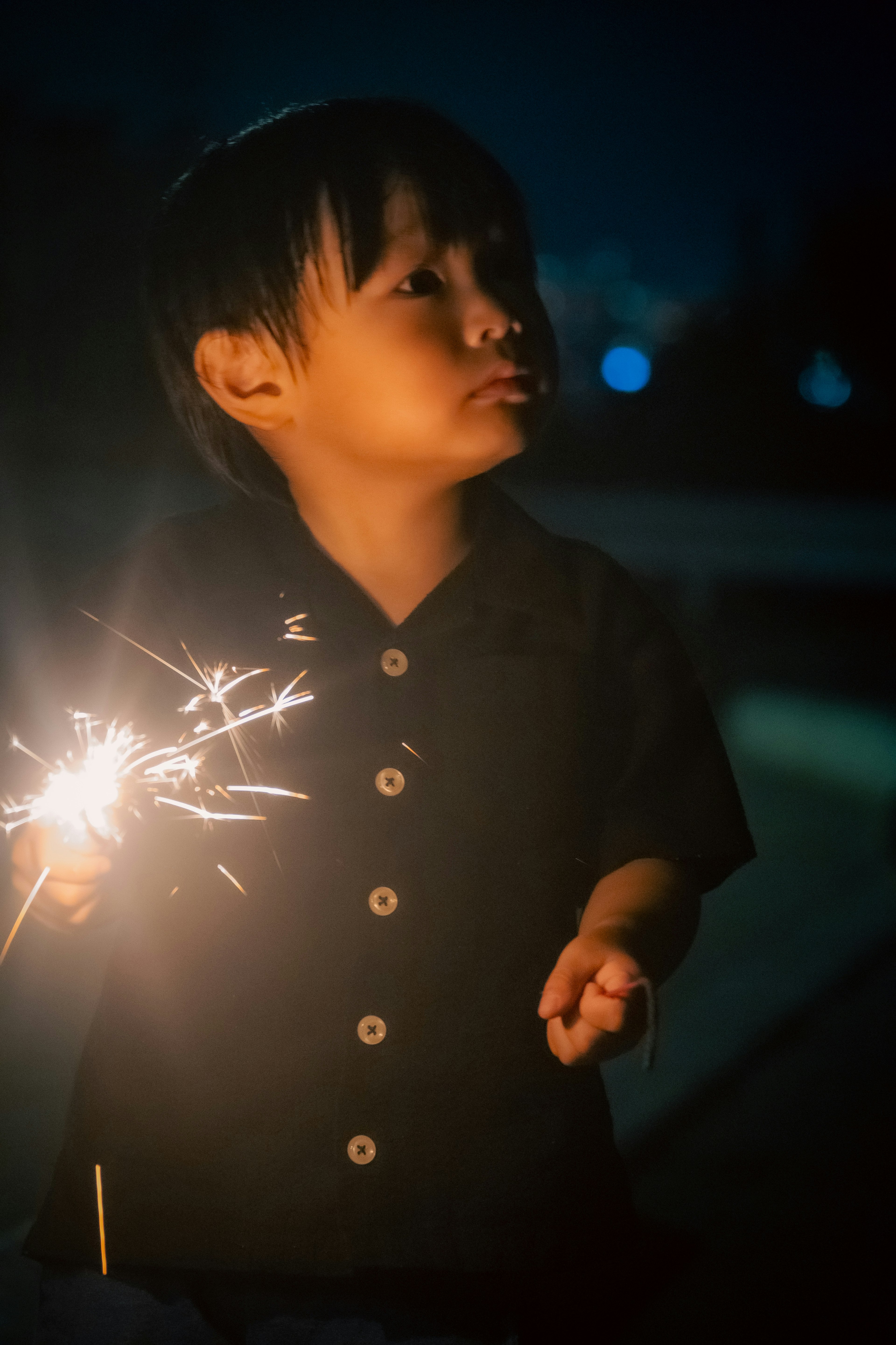 Side profile of a young boy holding a sparkler in the dark