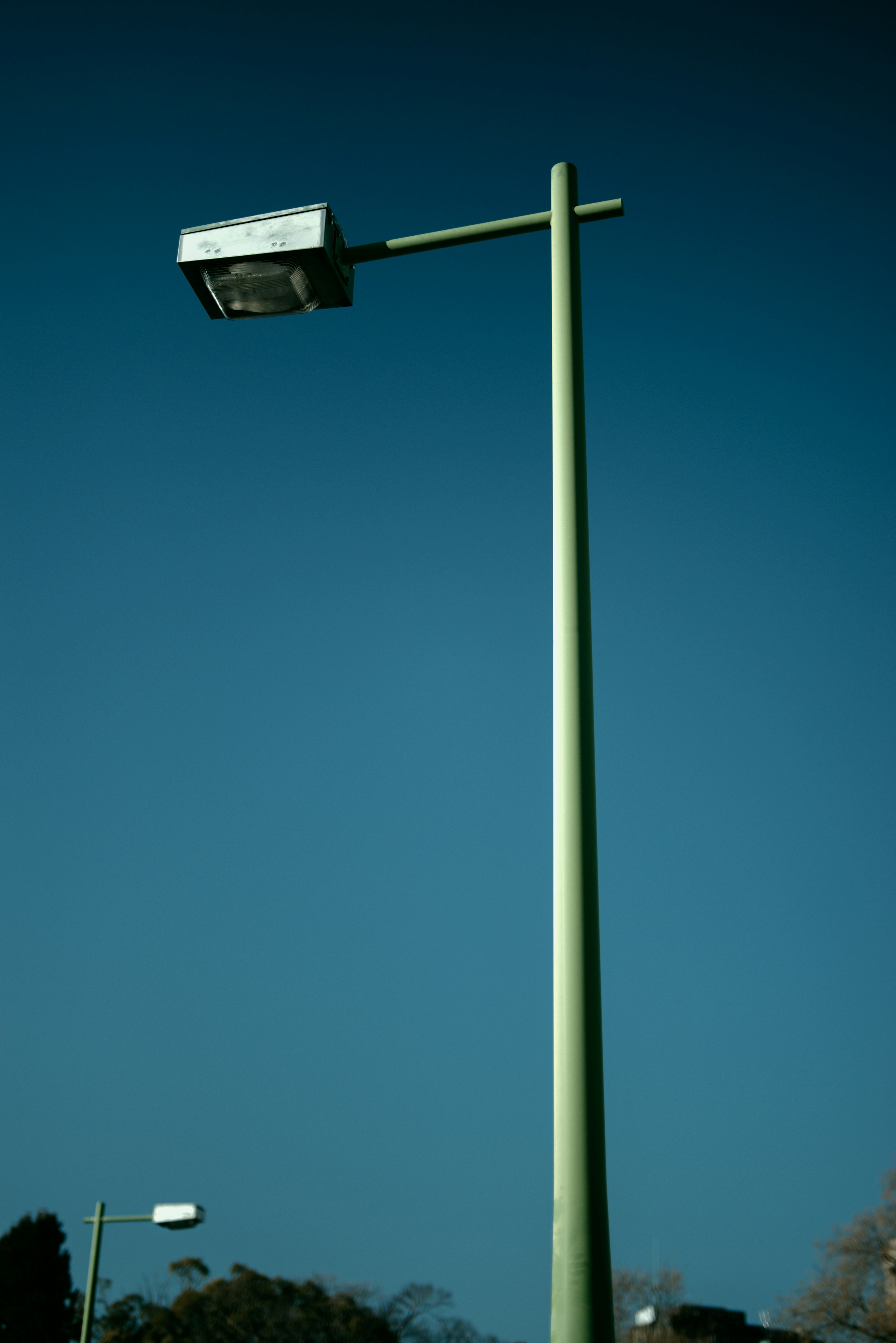 Grüner Straßenlaternenmast mit Lampe vor klarem blauen Himmel