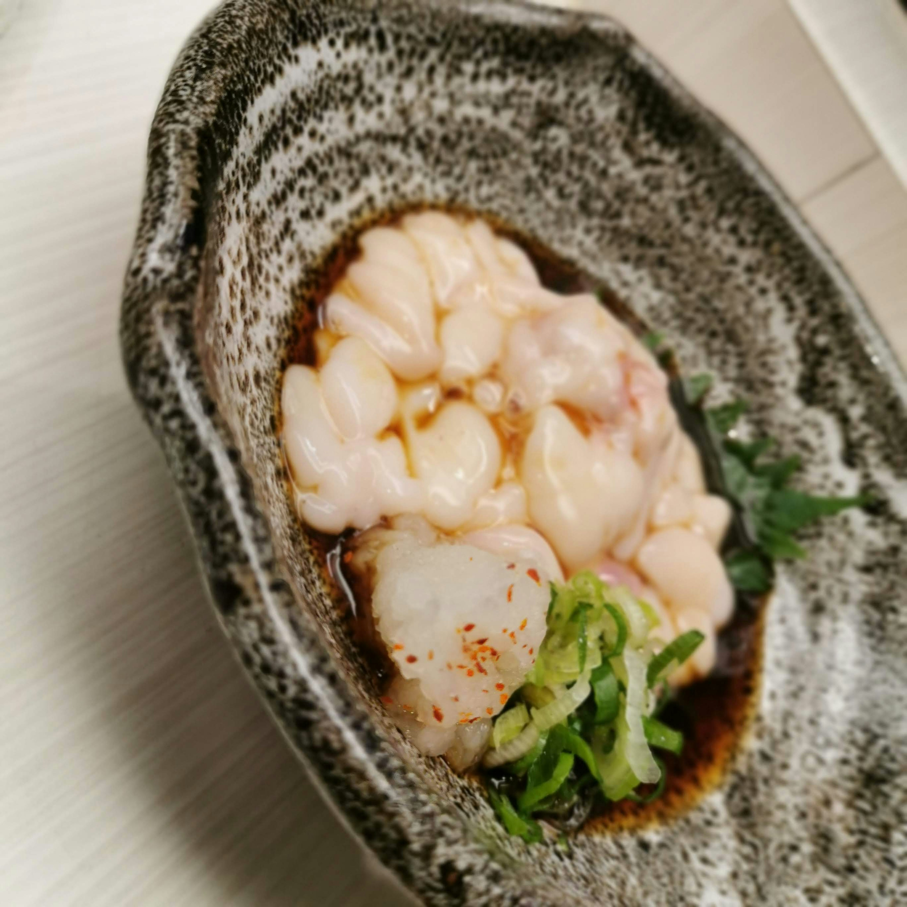 A dish of fresh seafood served in a small bowl with white flesh and green garnishes