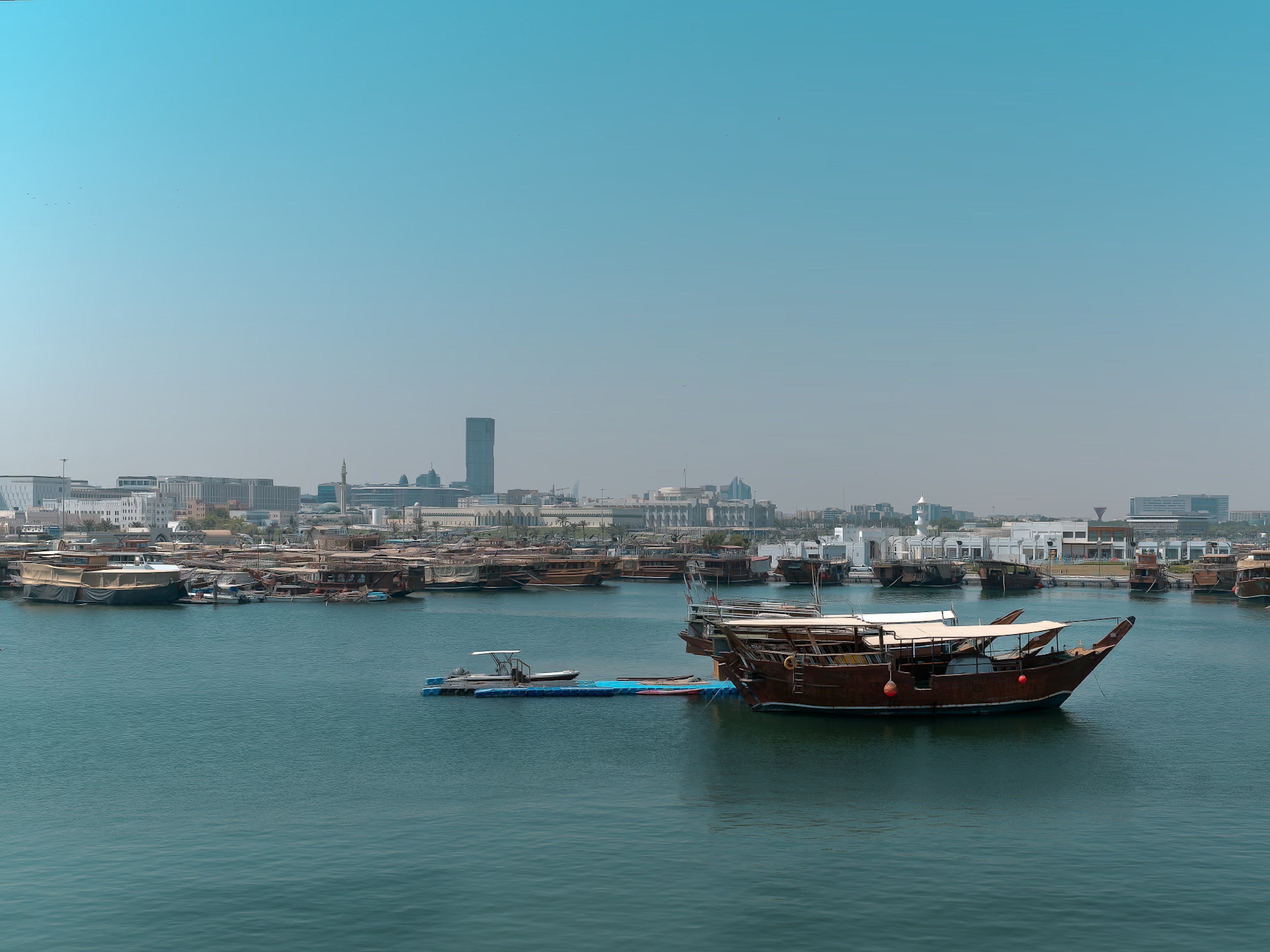 Traditional wooden Arabian dhow on water with modern city skyline in the background