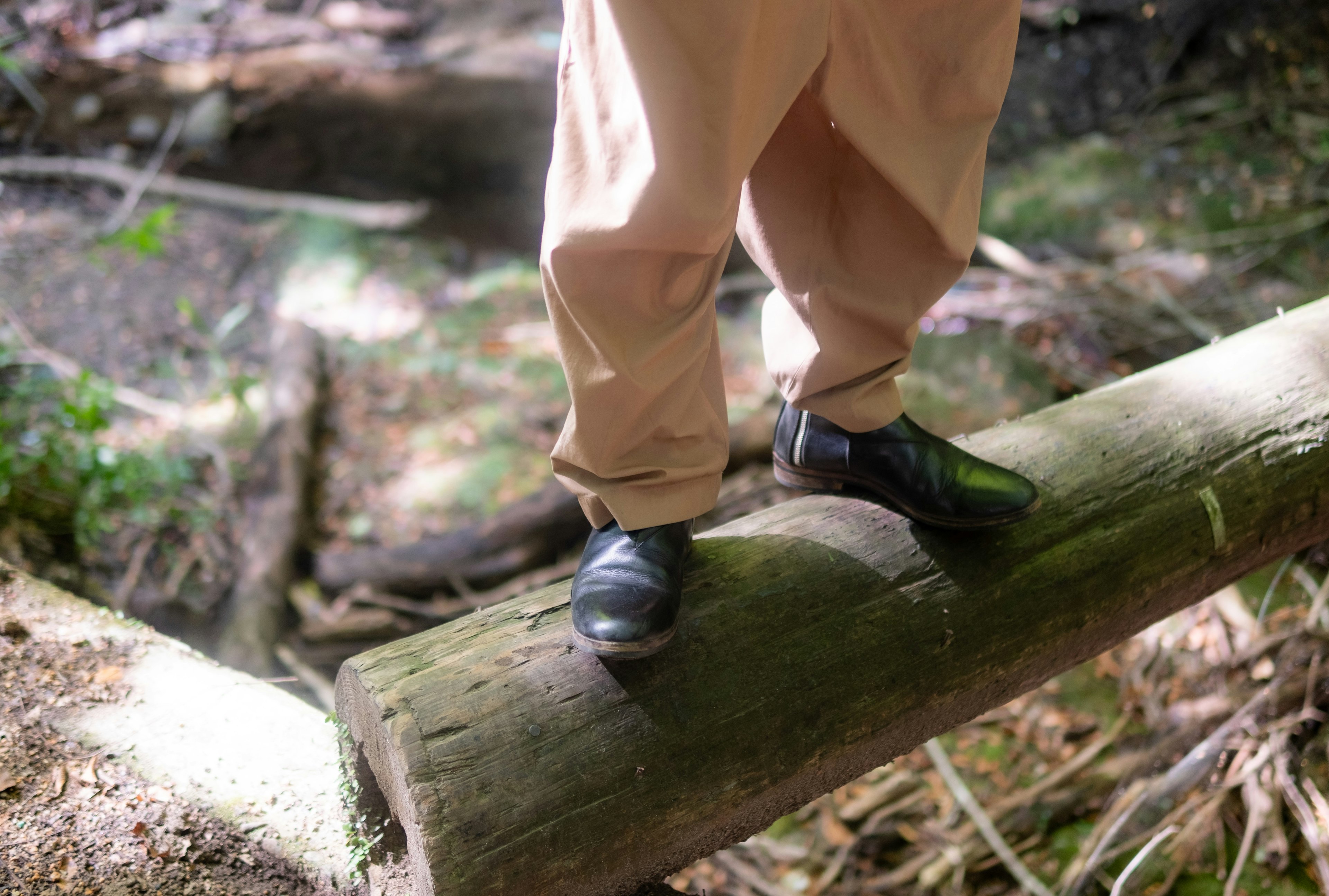 Feet standing on a log wearing light-colored pants and black shoes