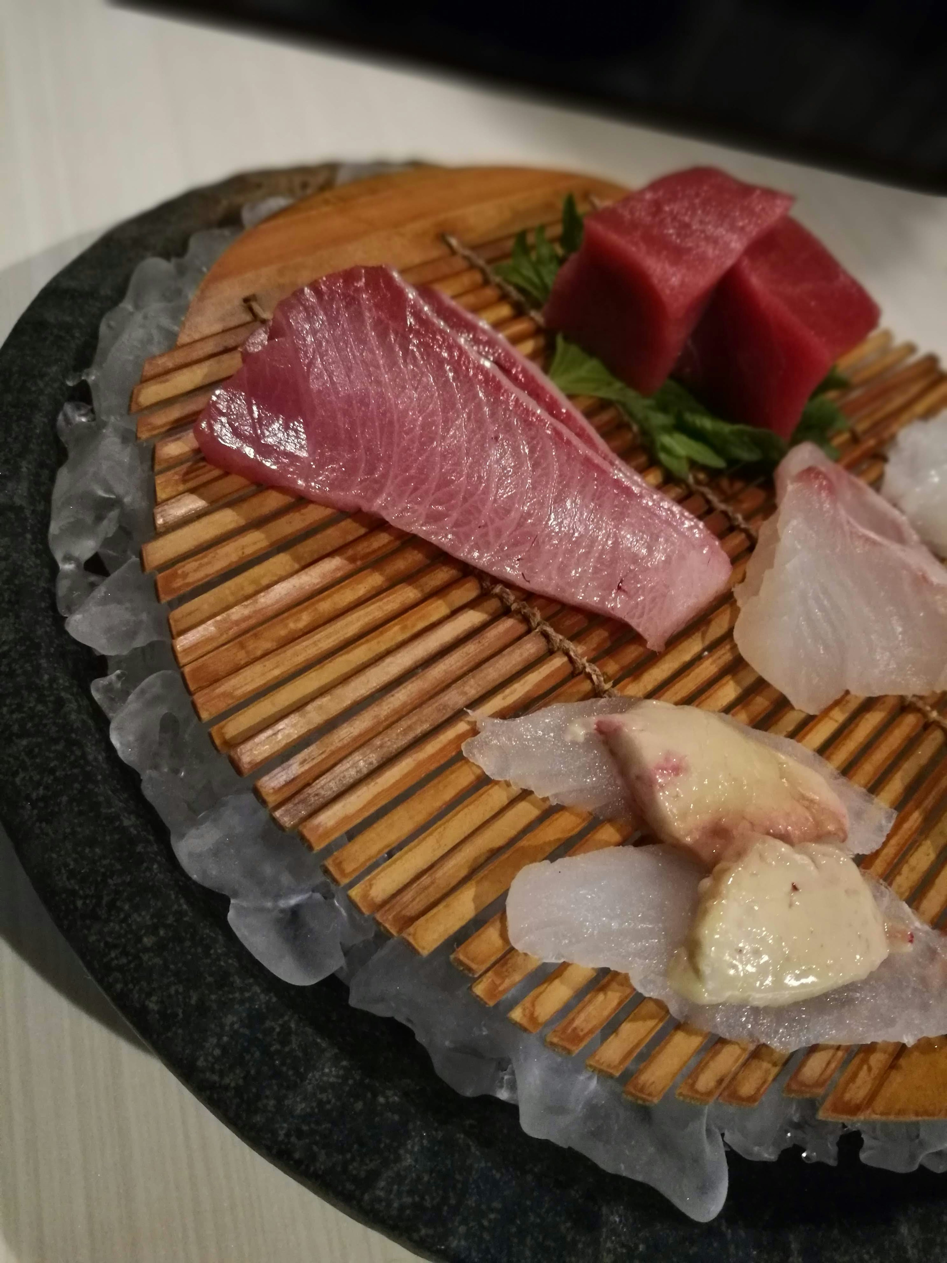 Una bandeja de sashimi fresco dispuesta sobre una tabla de madera sobre hielo