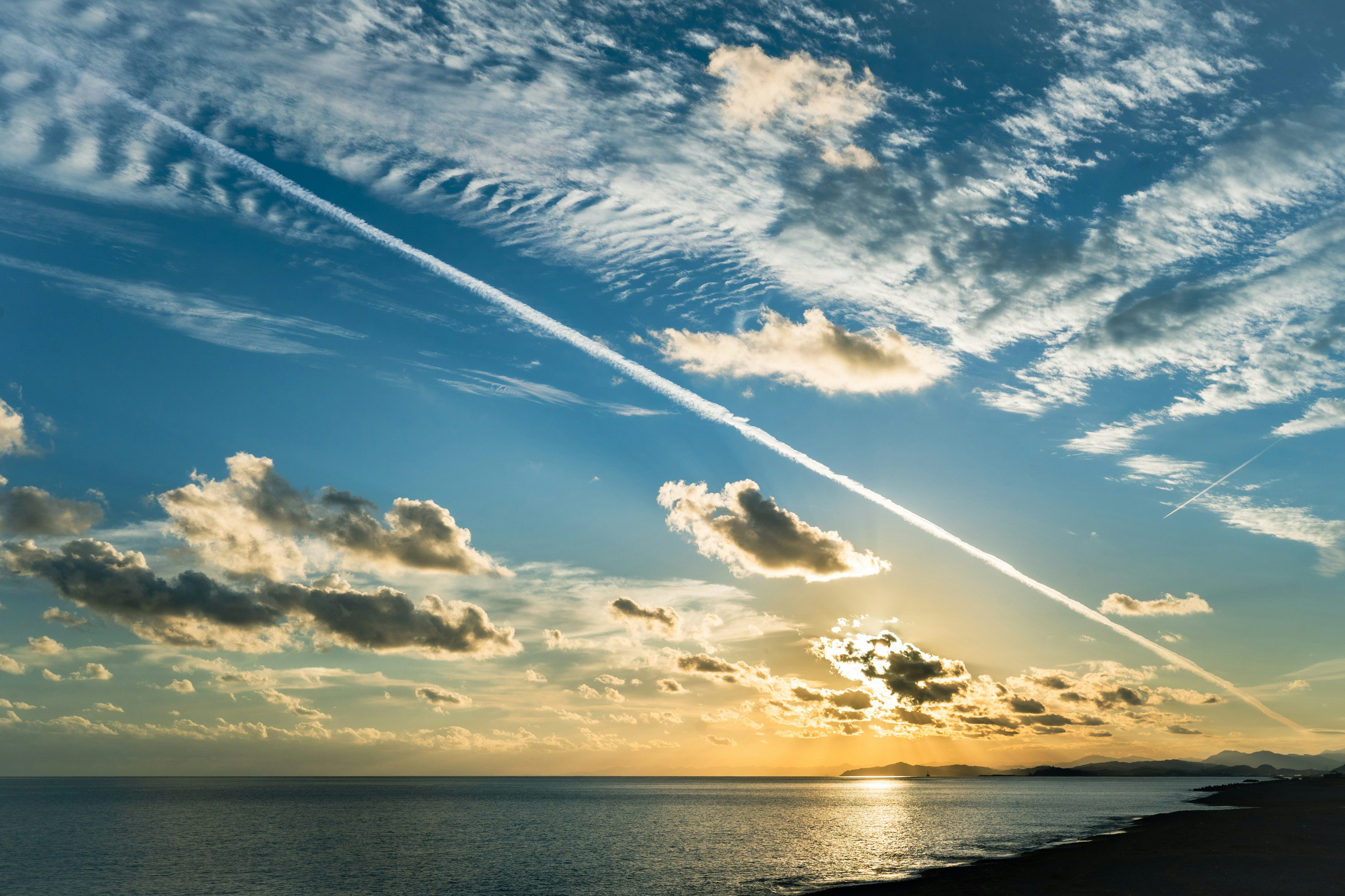 美しい夕日が映る海と空の景色 薄い雲と飛行機雲が広がる