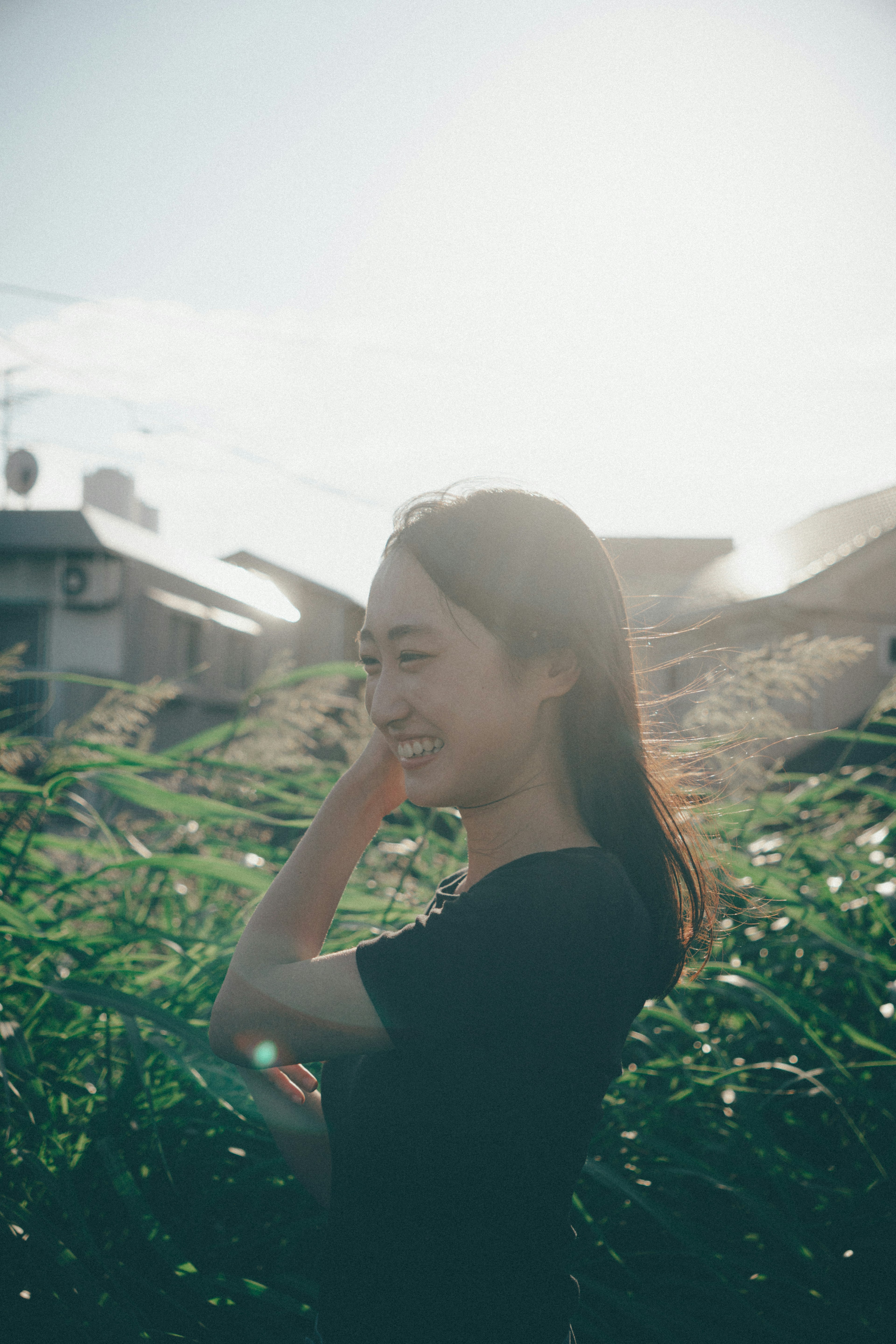 Una mujer sonriendo de perfil rodeada de hierba verde y cielo brillante