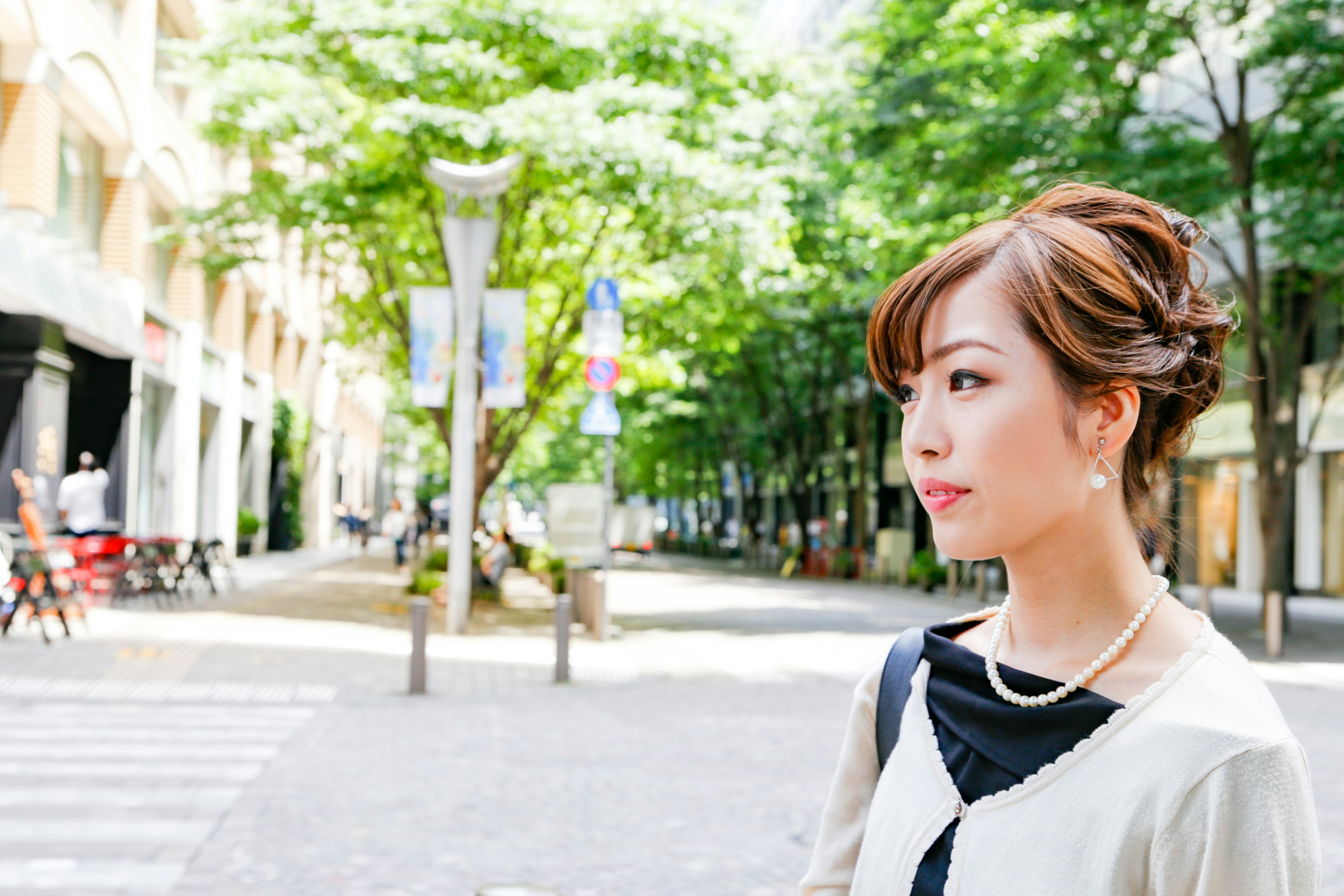 A woman standing on a street scene with green trees in the background and bright sunlight shining