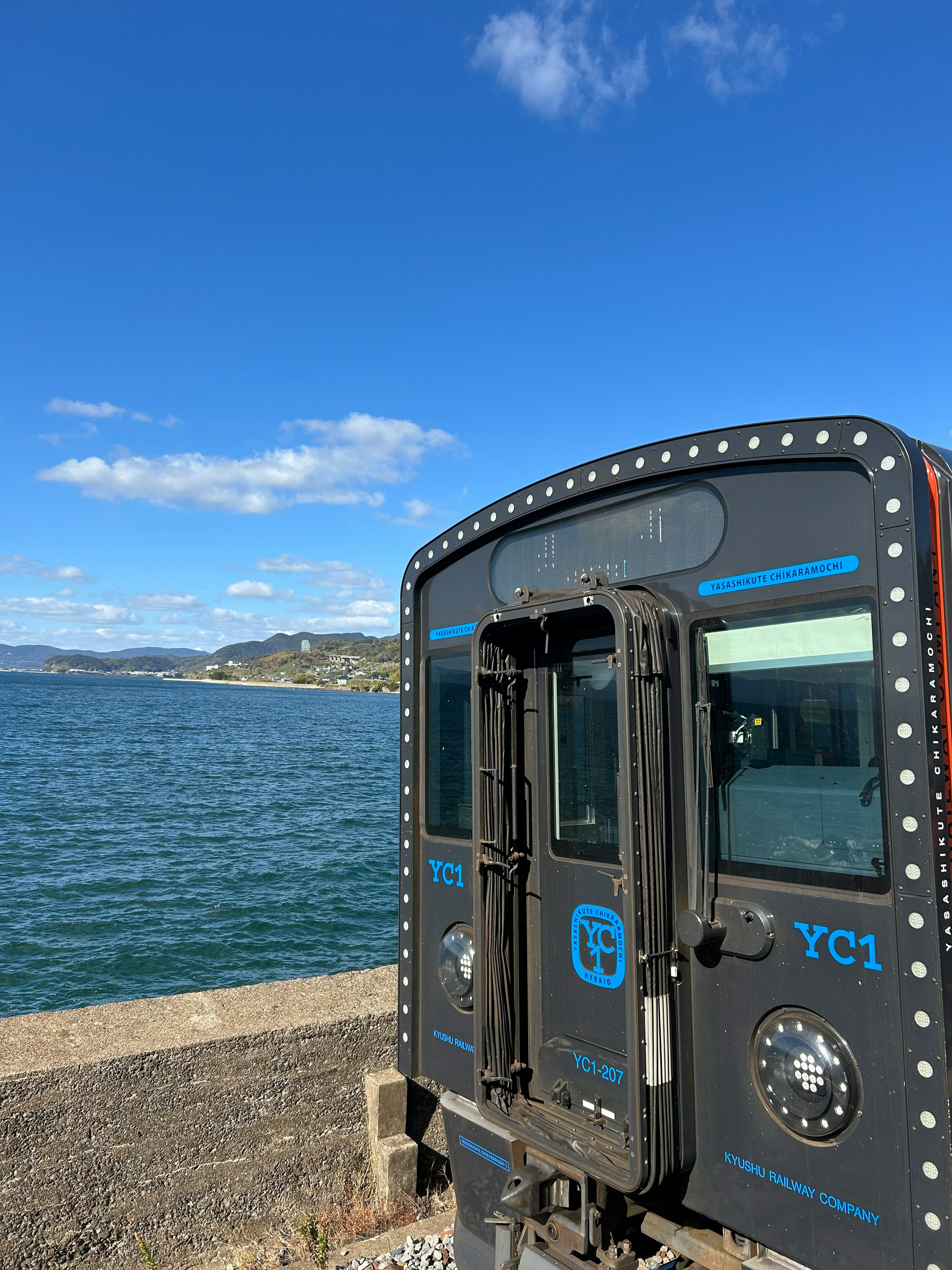 Seitenansicht eines Zuges am Meer mit klarem blauen Himmel und Wolken