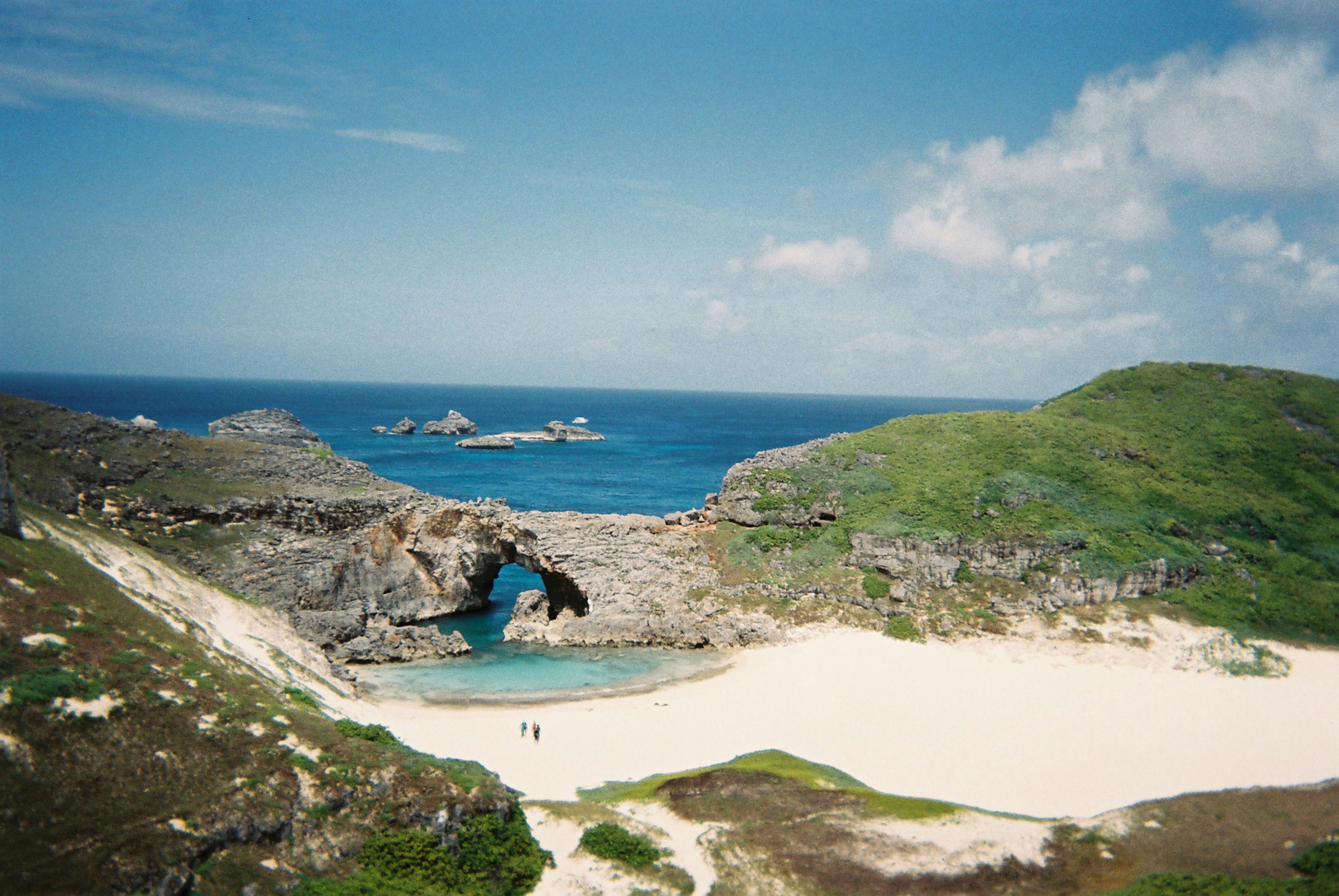 Vista panoramica di una spiaggia con acqua turchese circondata da colline verdi e formazioni rocciose