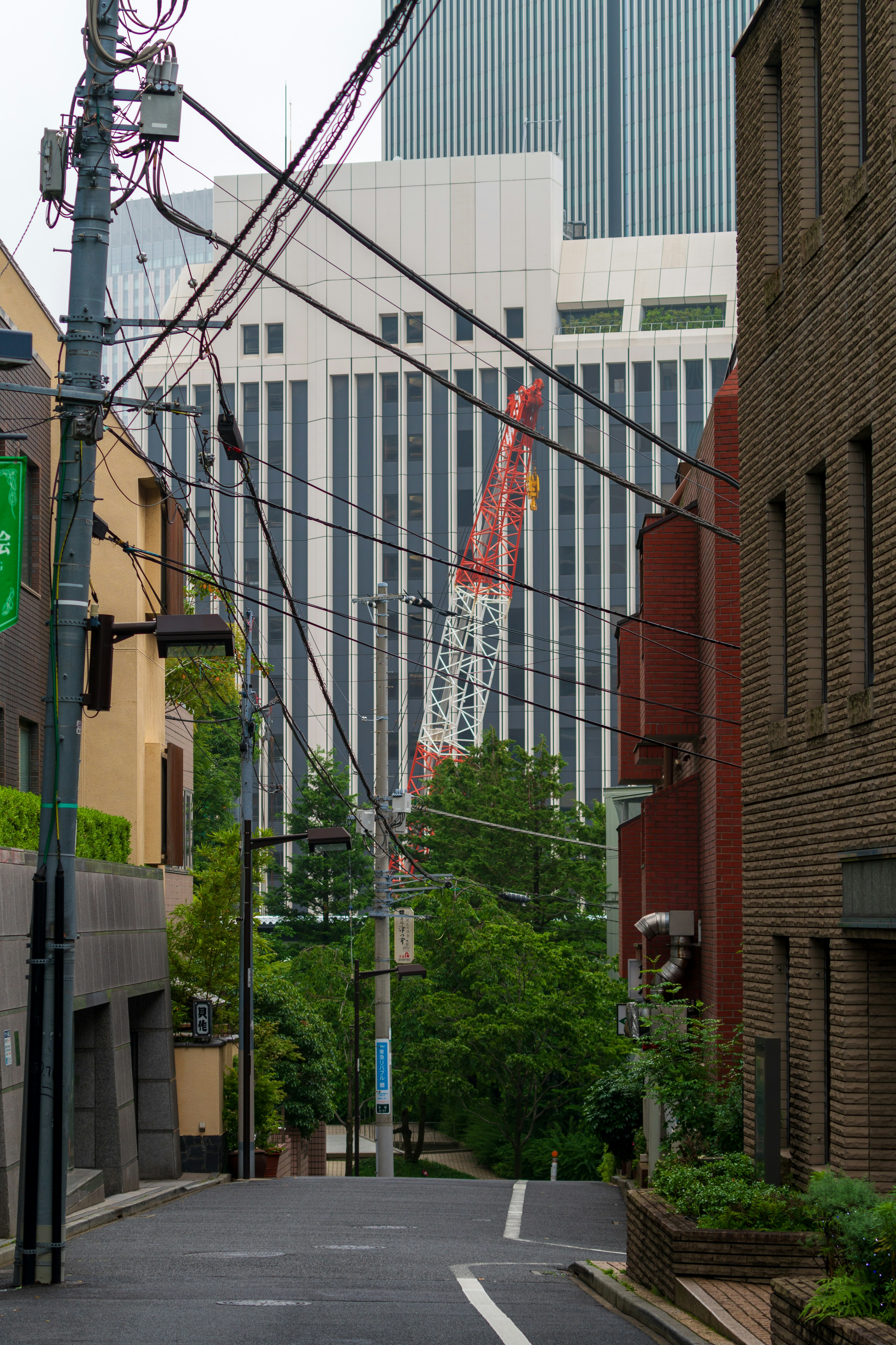 Narrow street lined with buildings and green trees Red crane visible on the facade of a tall building