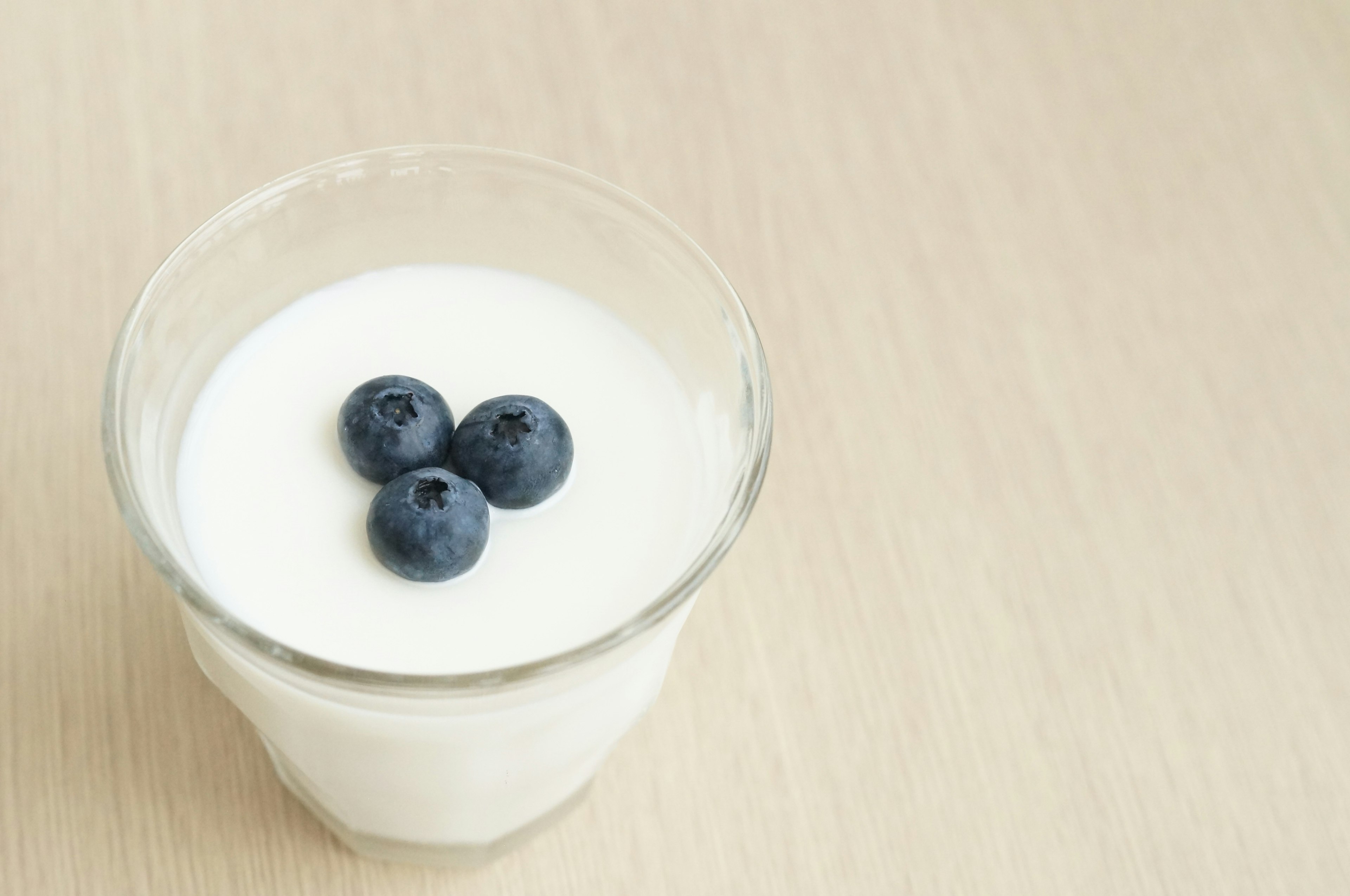 A glass of yogurt topped with three blueberries