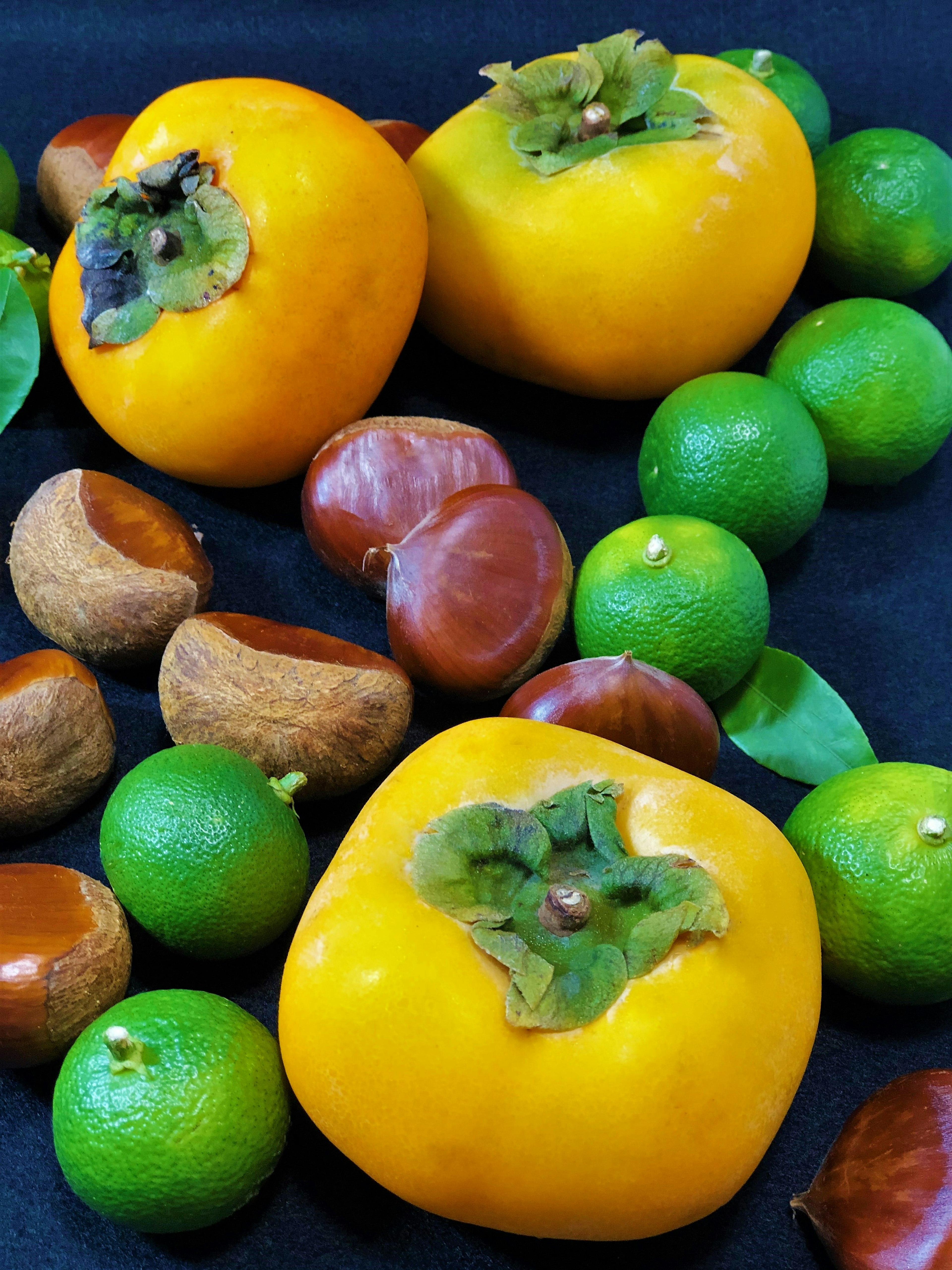 Bunte Anordnung von gelben Persimmons und grünen Limetten auf dunklem Hintergrund