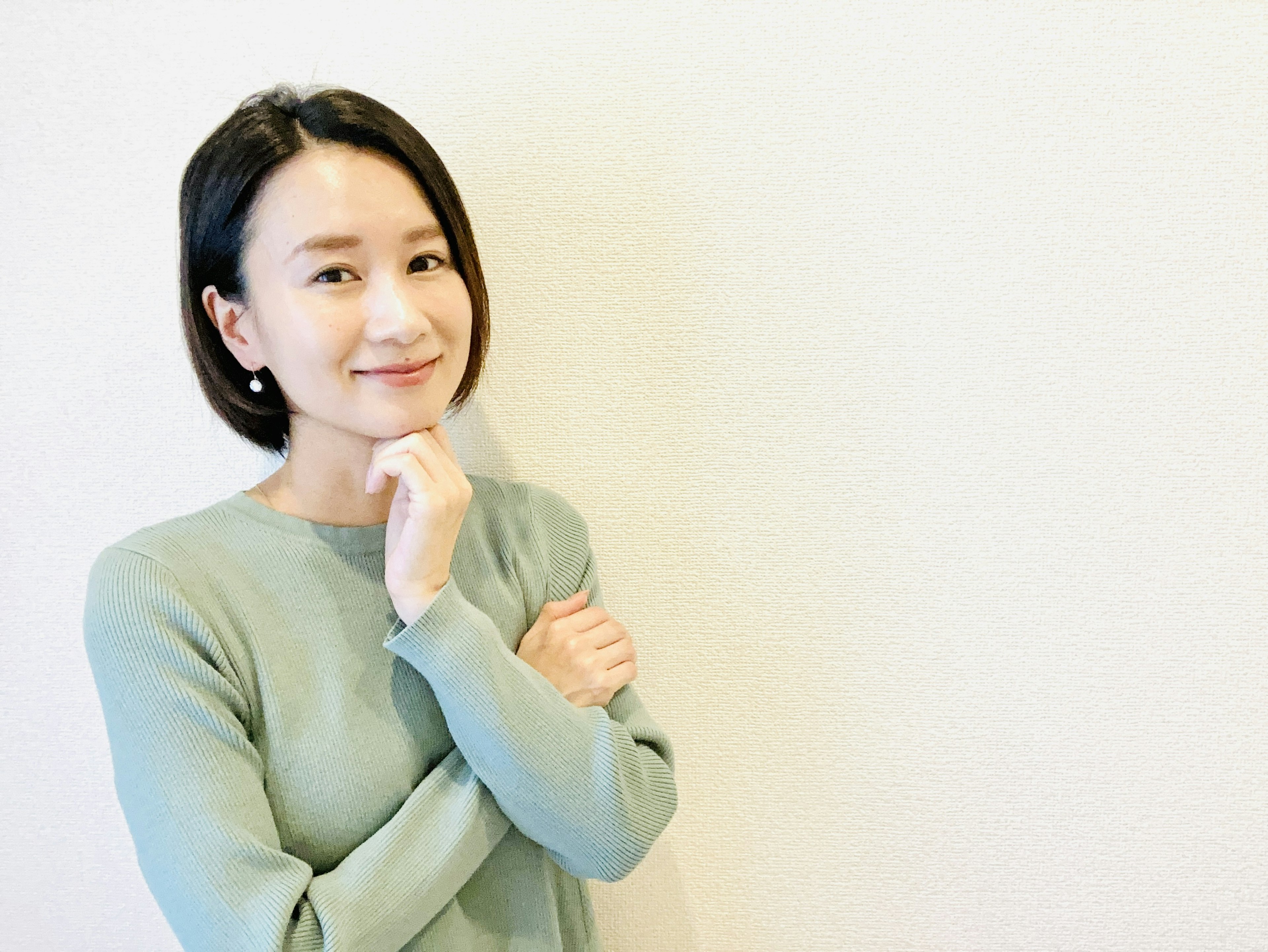 Portrait d'une femme souriante portant un pull vert sur fond blanc