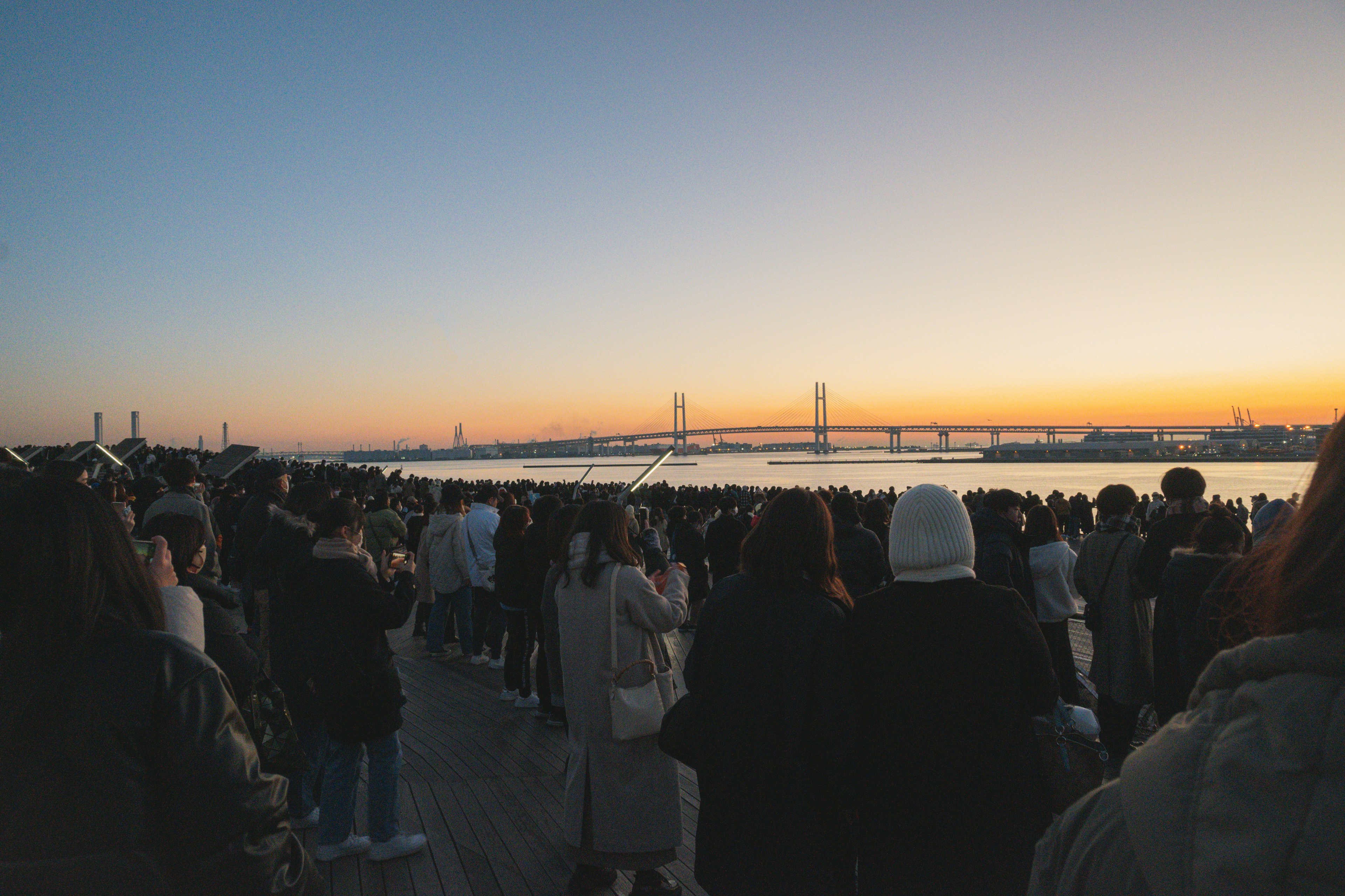 Multitud de personas reunidas al atardecer con un puente de fondo