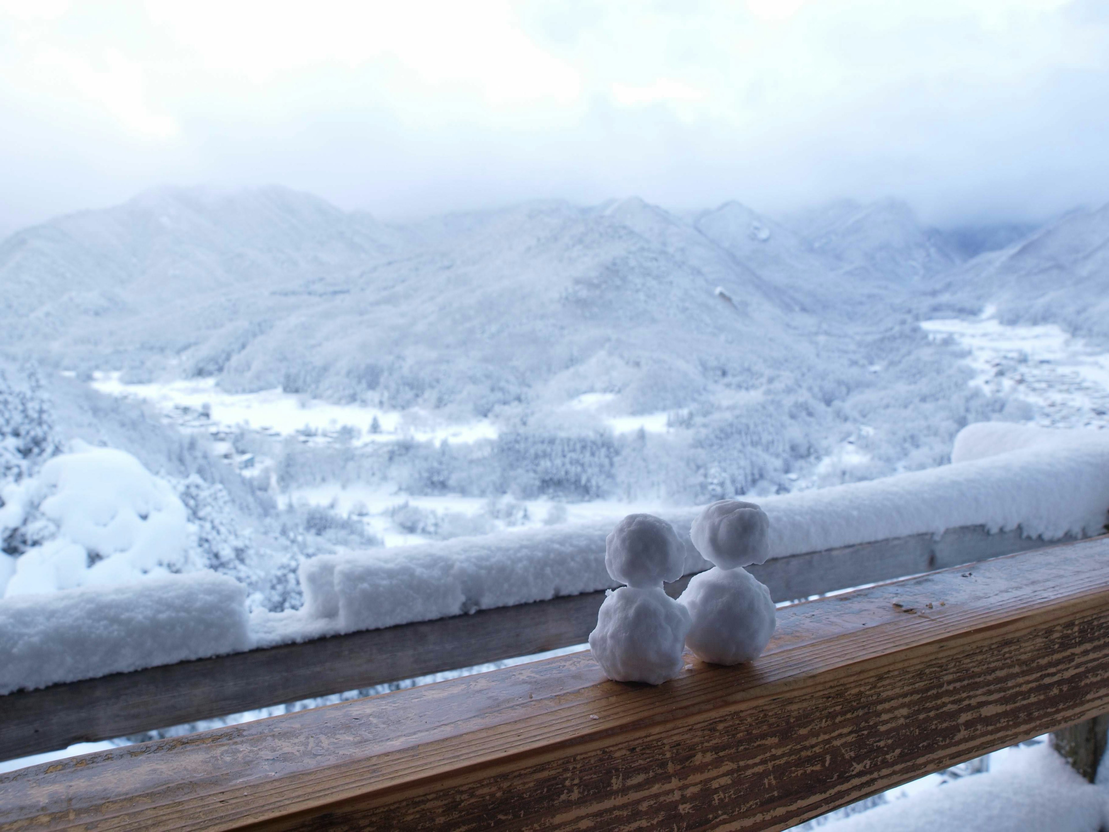 Ein Paar Schneemänner sitzt auf einer Holzbank mit einer verschneiten Landschaft im Hintergrund