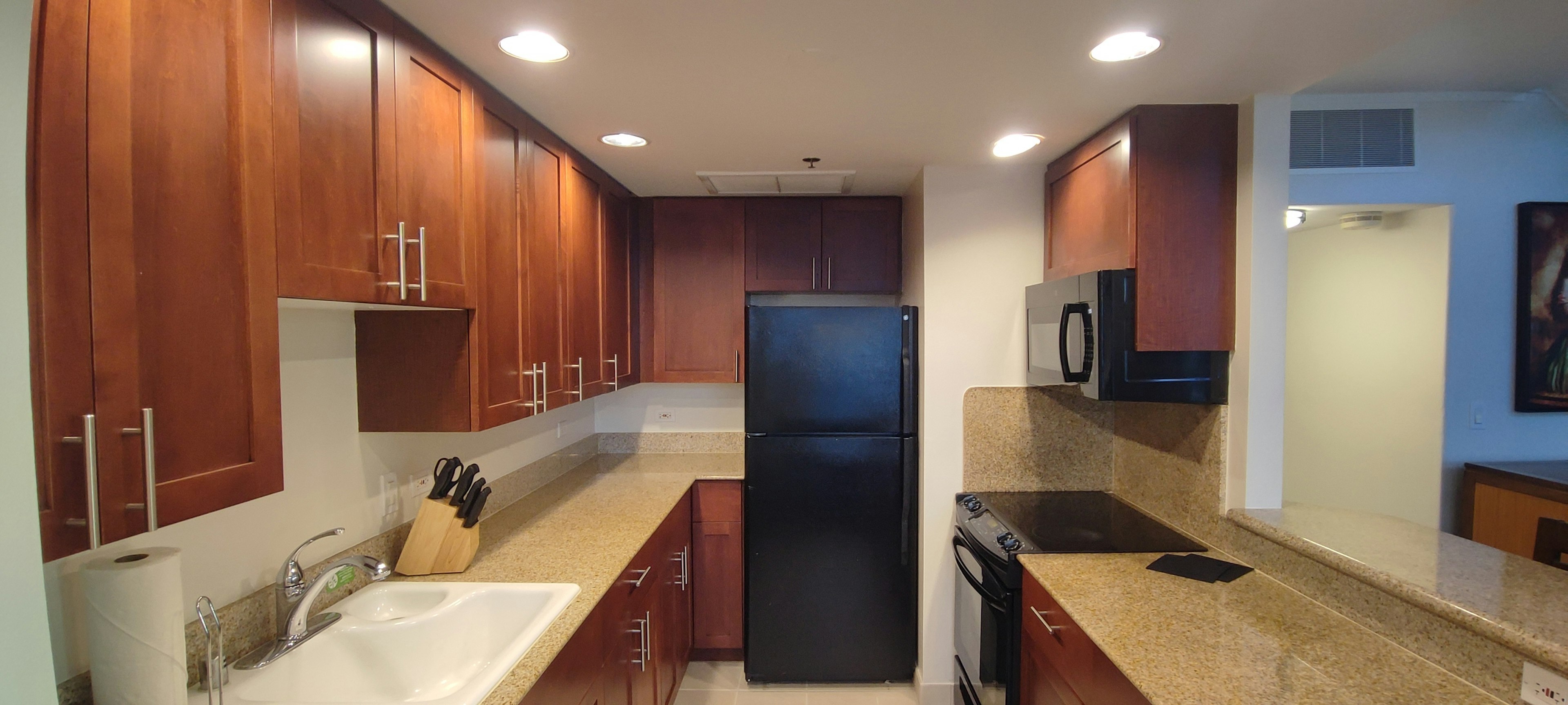 Diseño de cocina moderna con armarios de madera cálida refrigerador negro y electrodomésticos encimeras de color crema