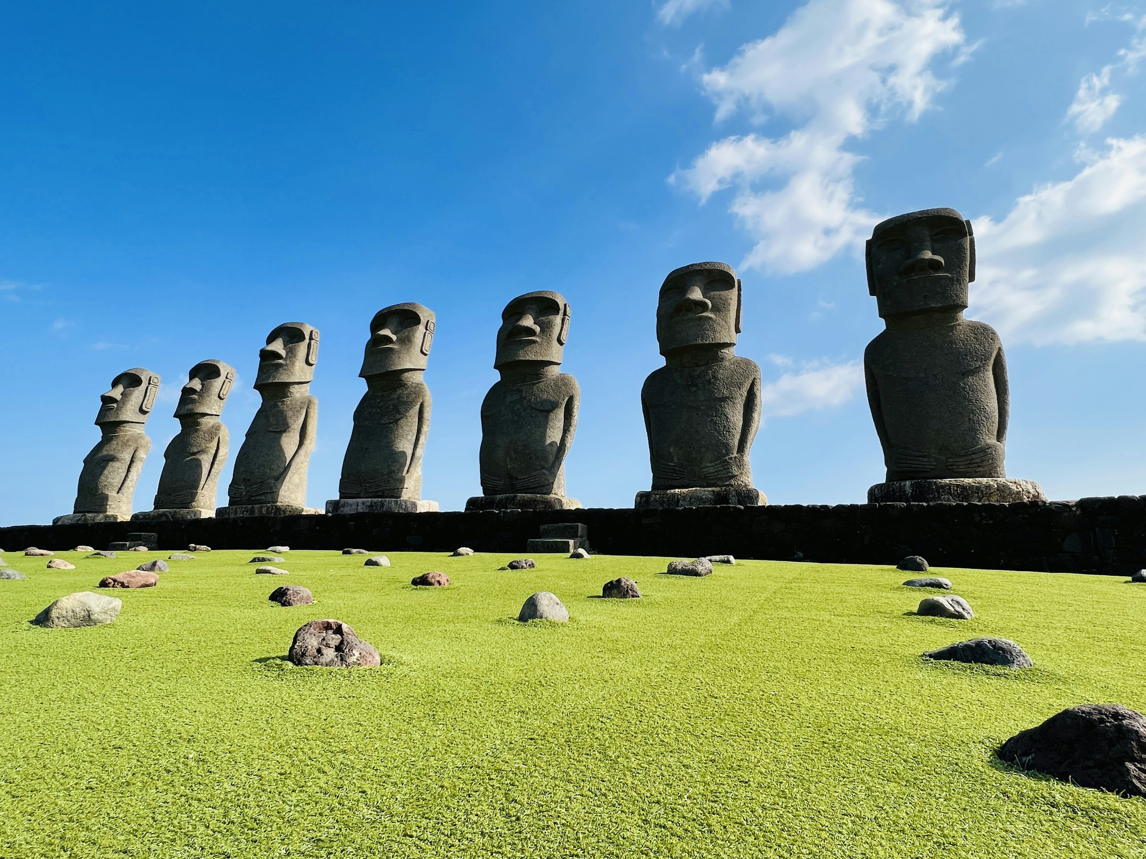 Reihe von Moai-Statuen auf der Osterinsel vor blauem Himmel und grünem Gras