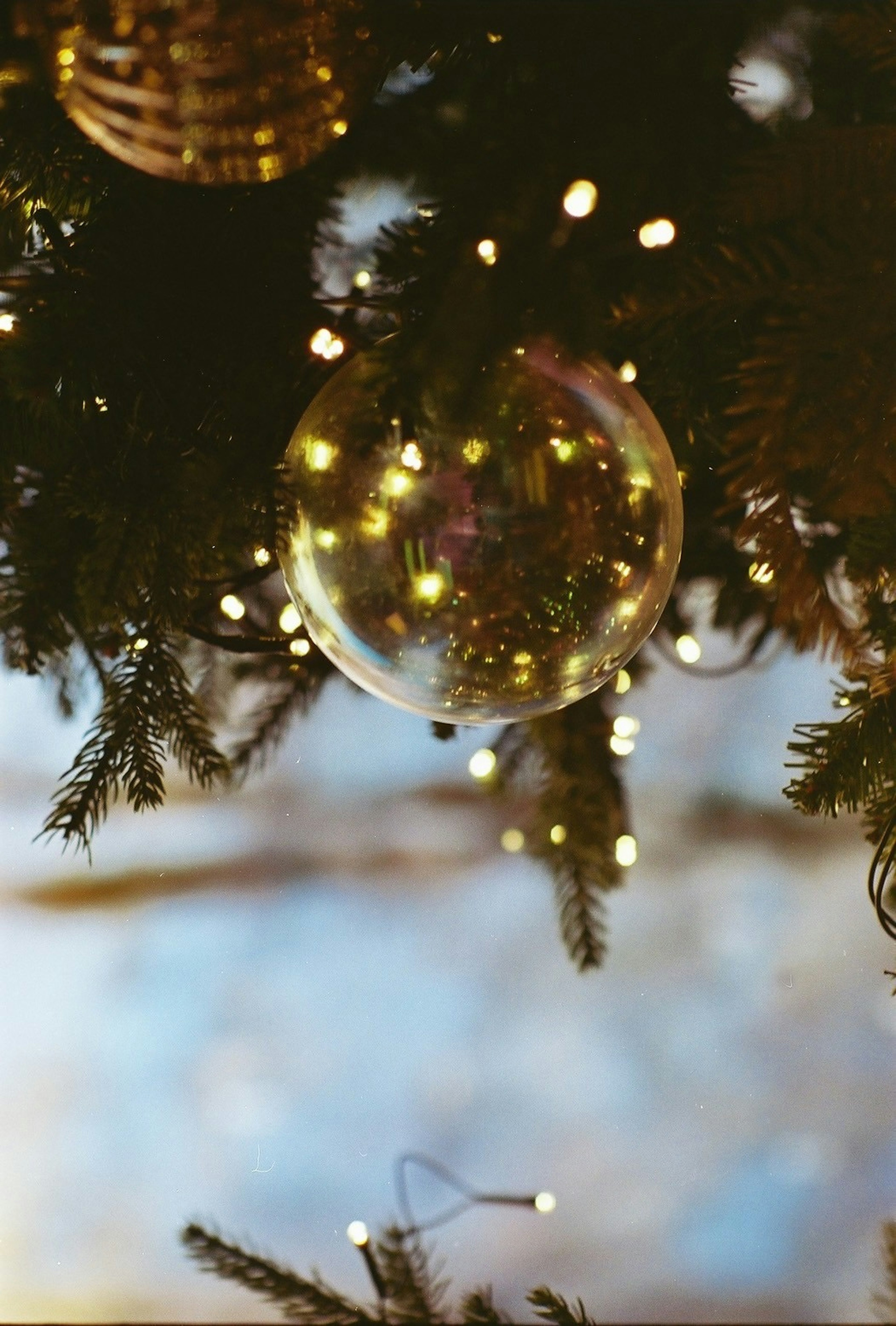 Funkelndes Ornament an einem Weihnachtsbaum mit sanft verschwommenem blauen Himmel im Hintergrund