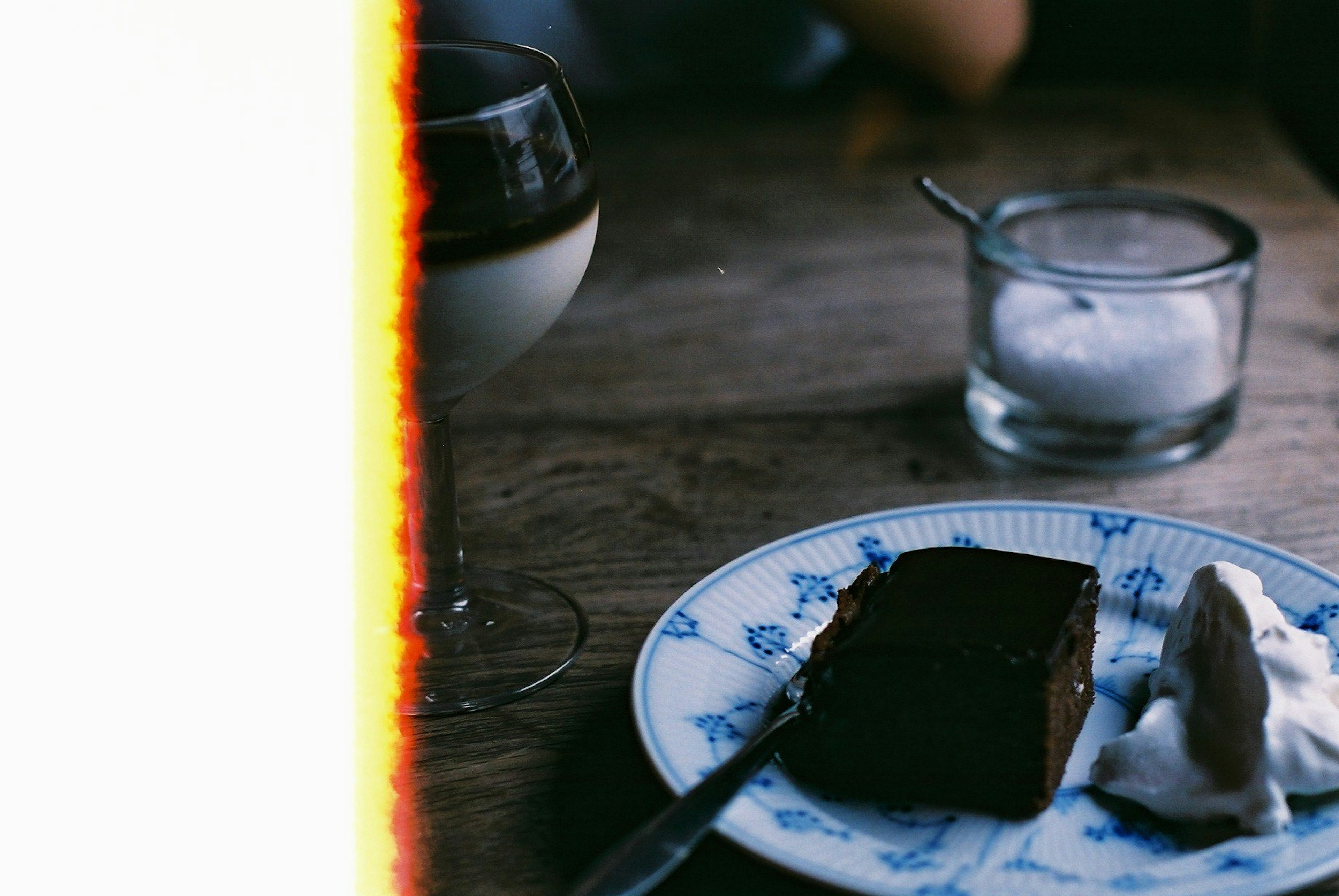 Pastel de chocolate en un plato decorativo con crema batida y un vaso de postre