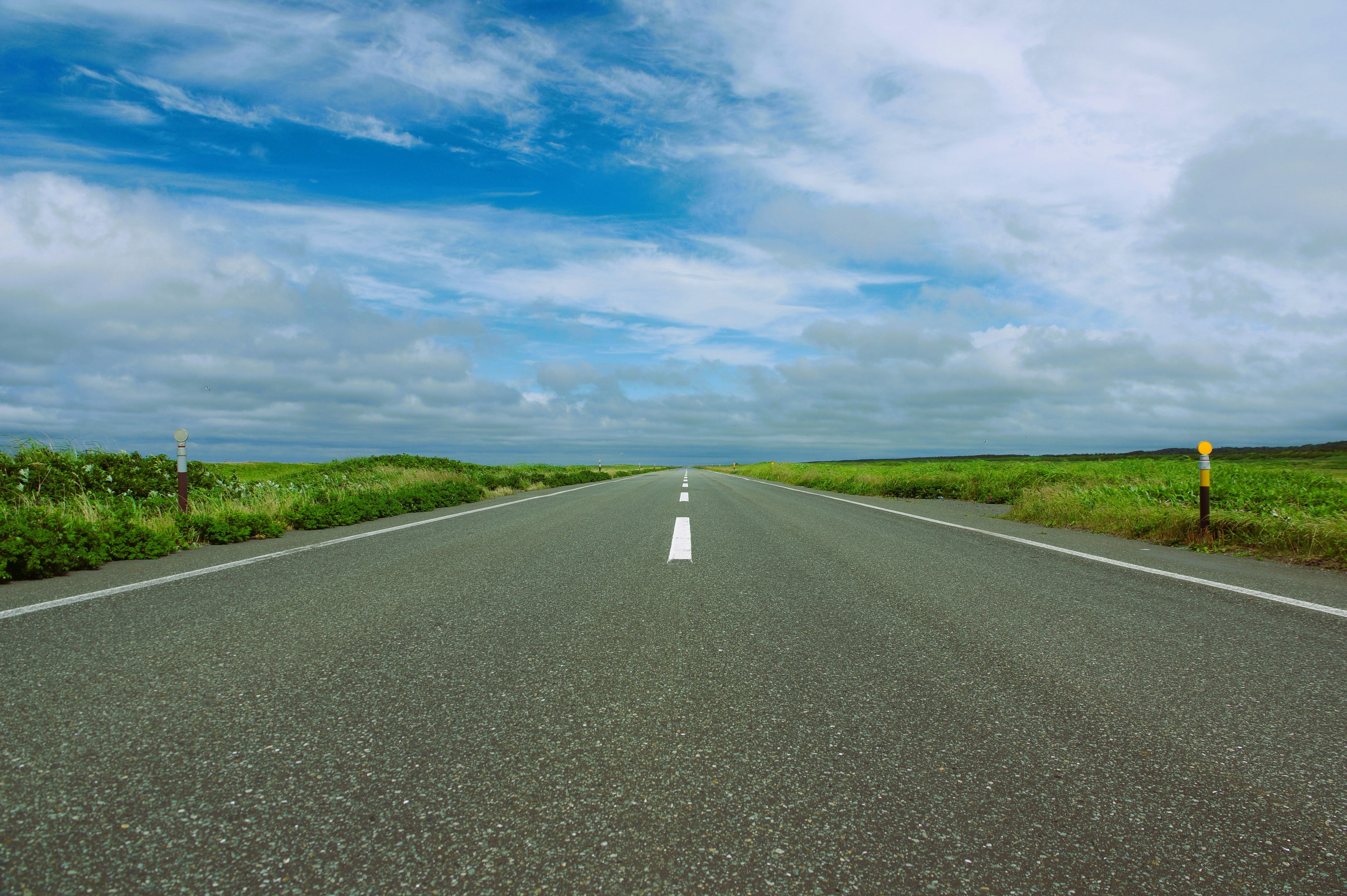 Carretera recta rodeada de campos verdes y cielo azul