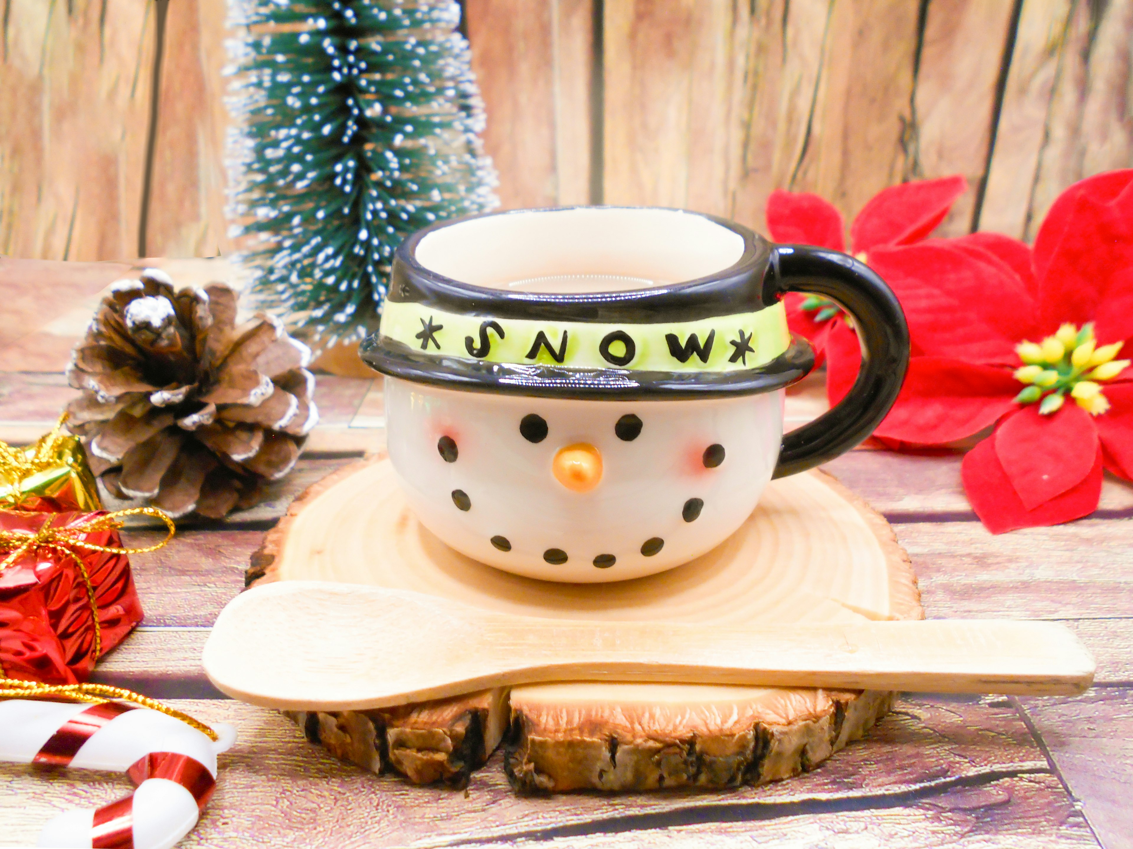 A snowman face cup with a spoon placed on a wooden plate