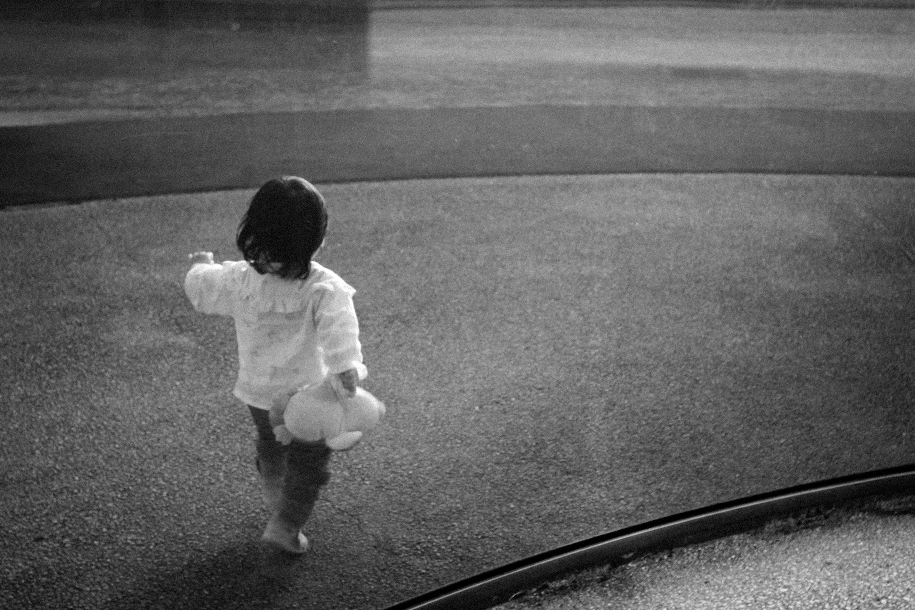 Black and white photo of a child walking in a park holding a stuffed animal