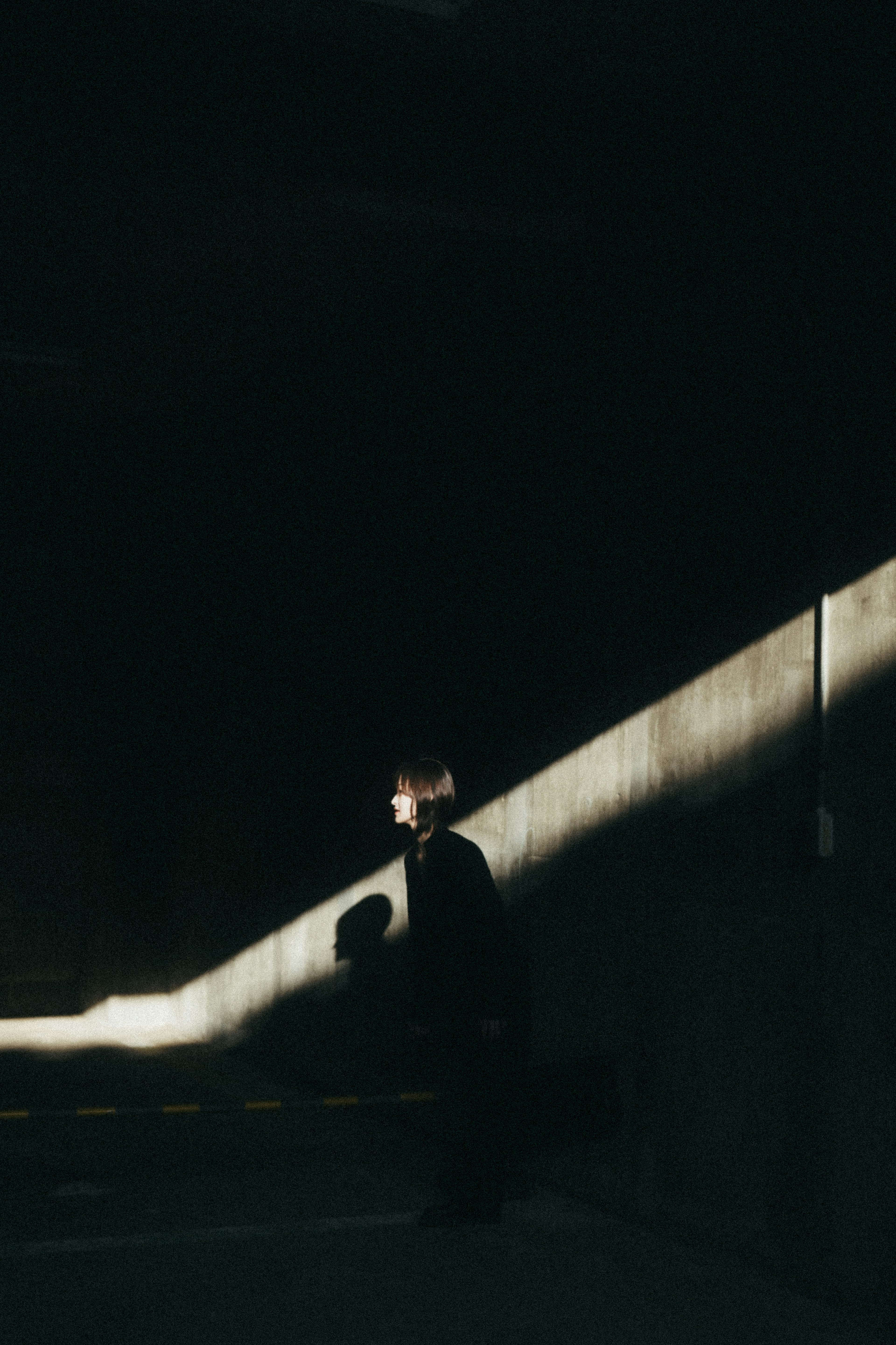 A person standing against a dark background with light casting on the wall