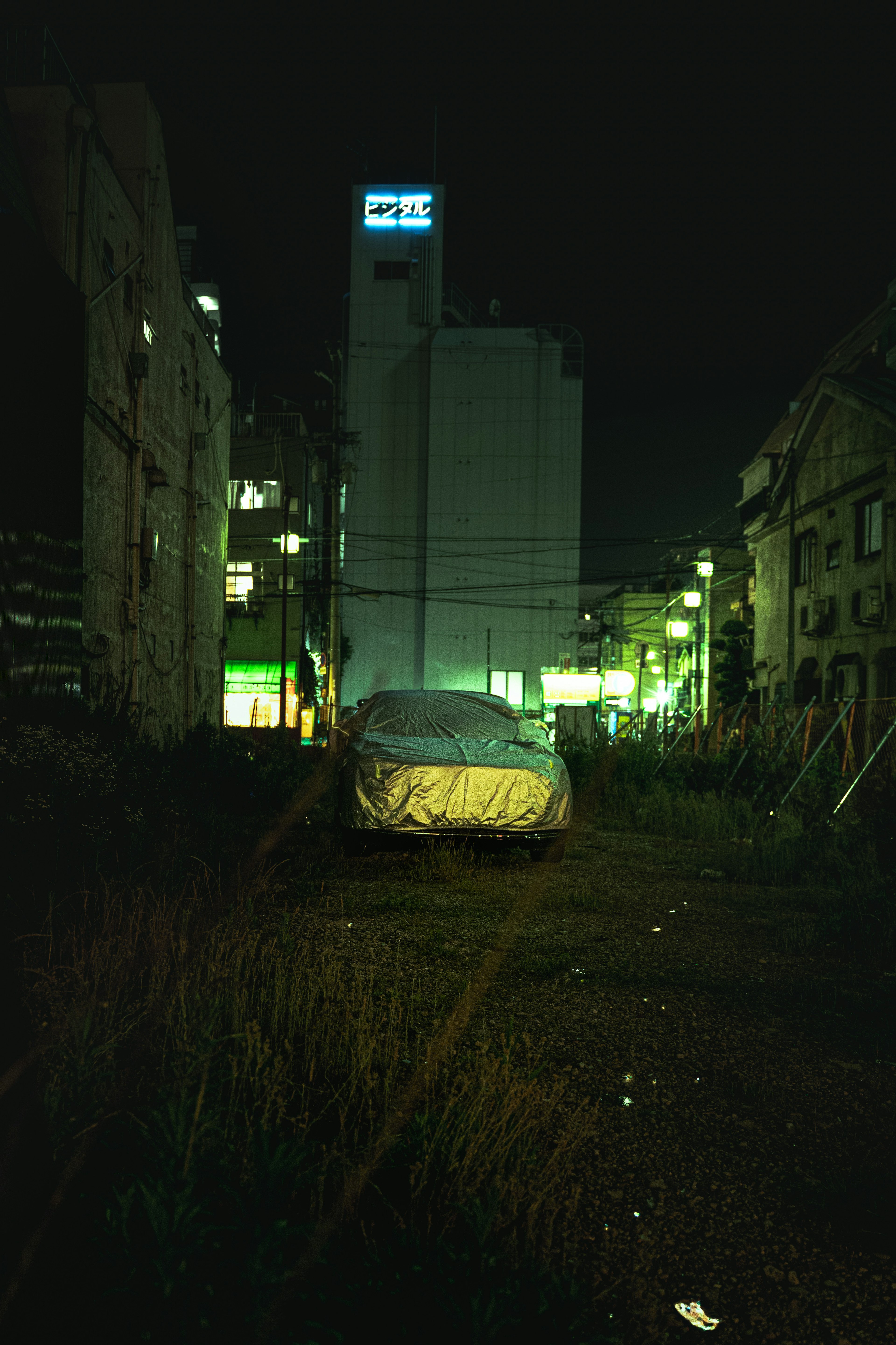 Covered car in an urban alley at night with surrounding buildings