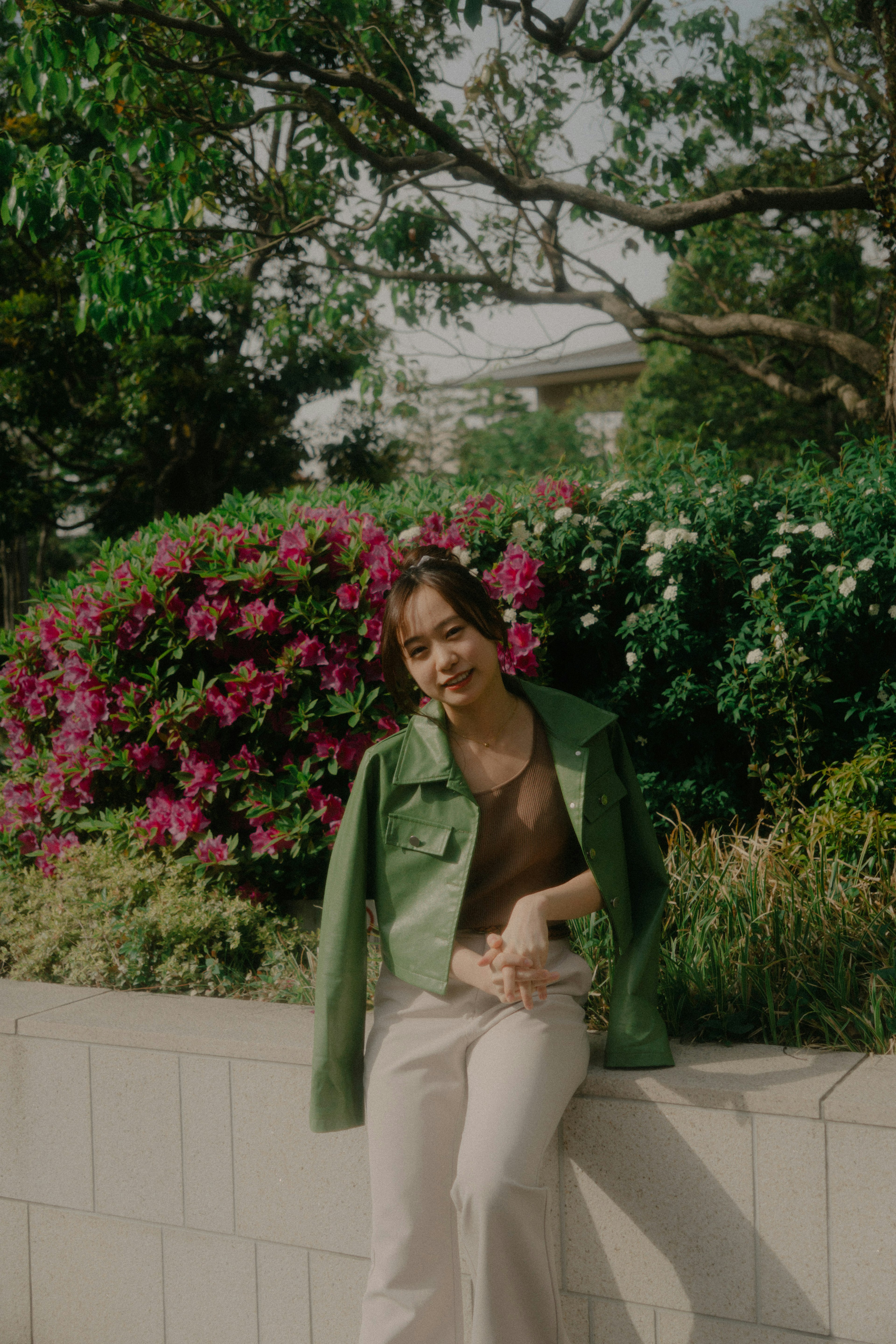 A woman in a green jacket smiling in front of flowers