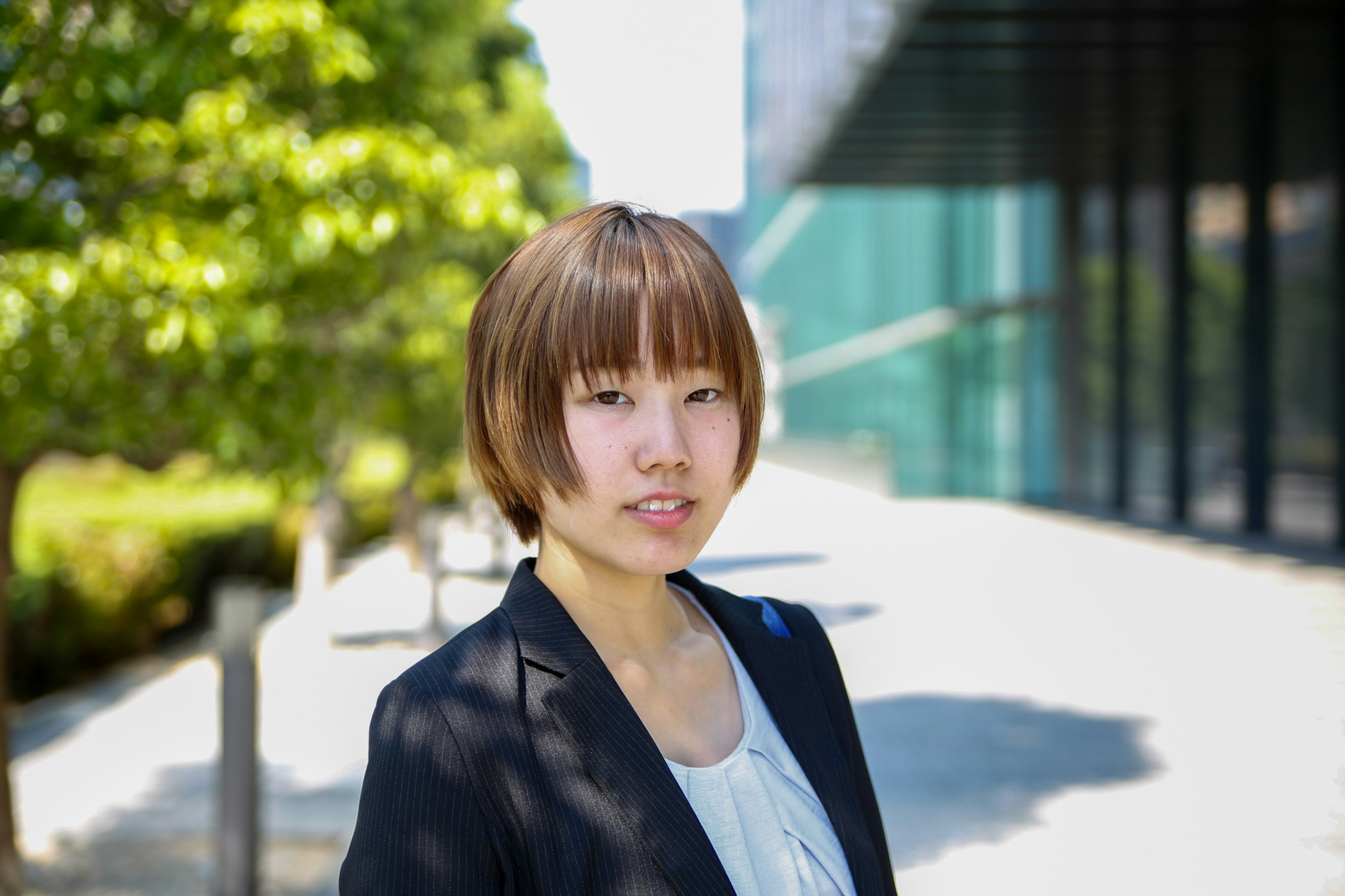 Young woman in a business suit with a modern building and greenery in the background