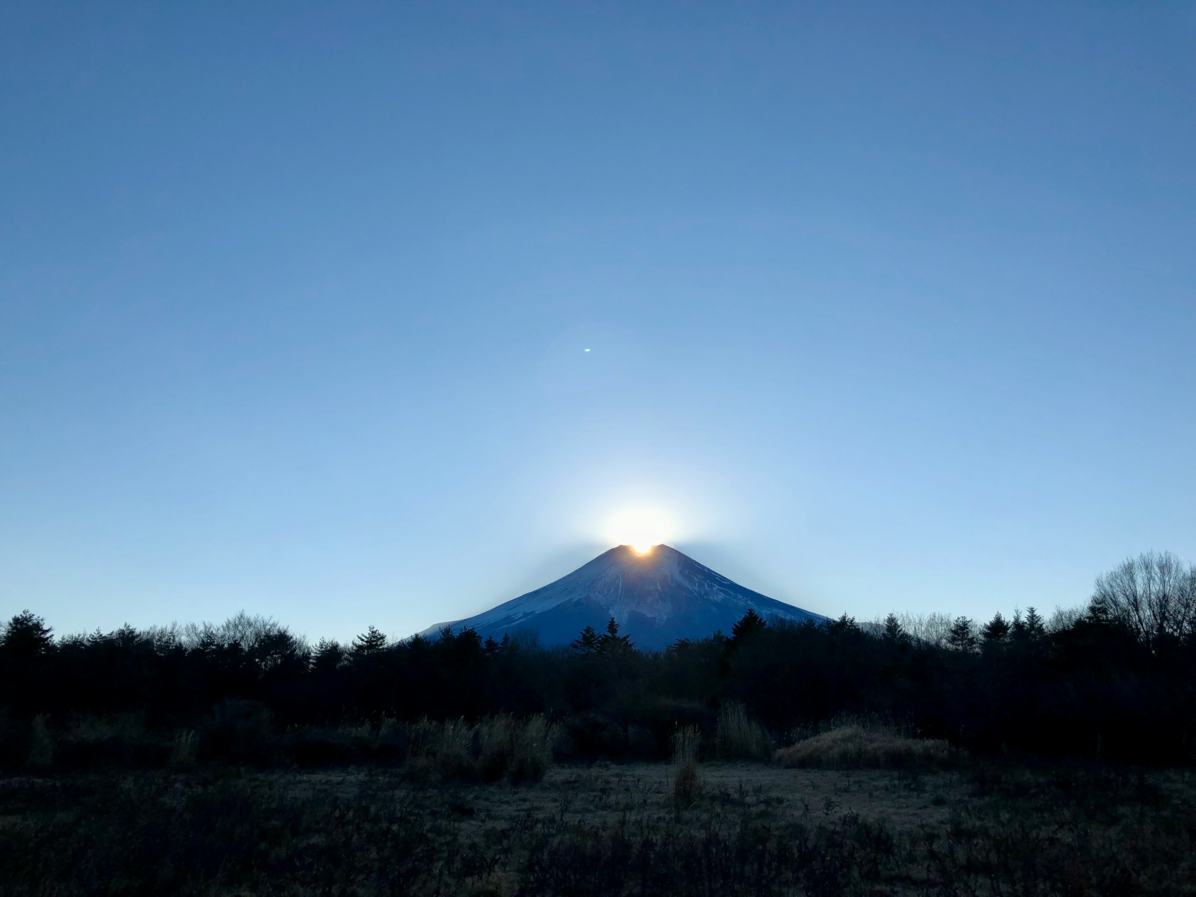 青空にそびえる富士山の頂上から昇る朝日