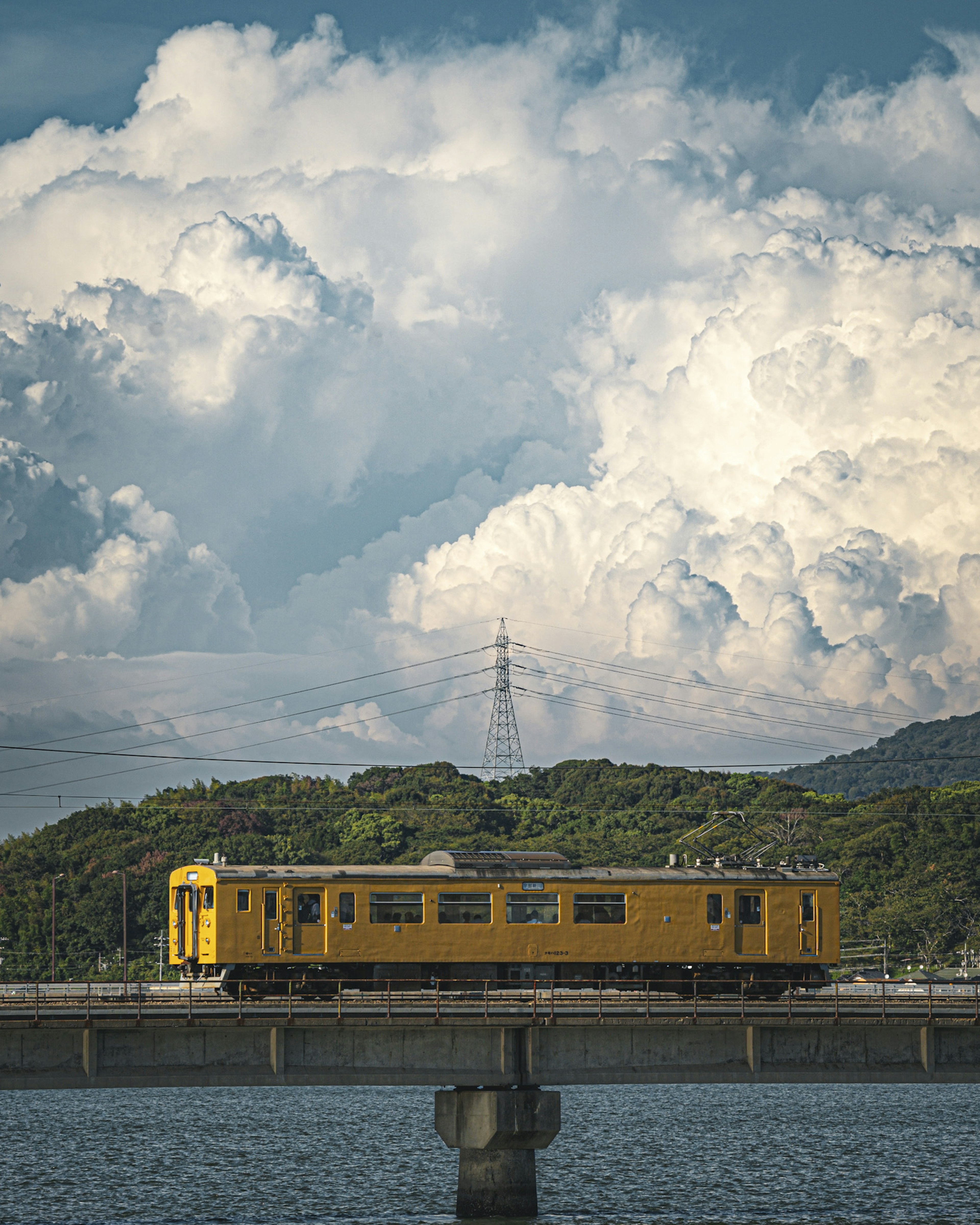 Ein gelber Zug, der auf einer Brücke vor einer Kulisse aus Wolken und Hügeln fährt