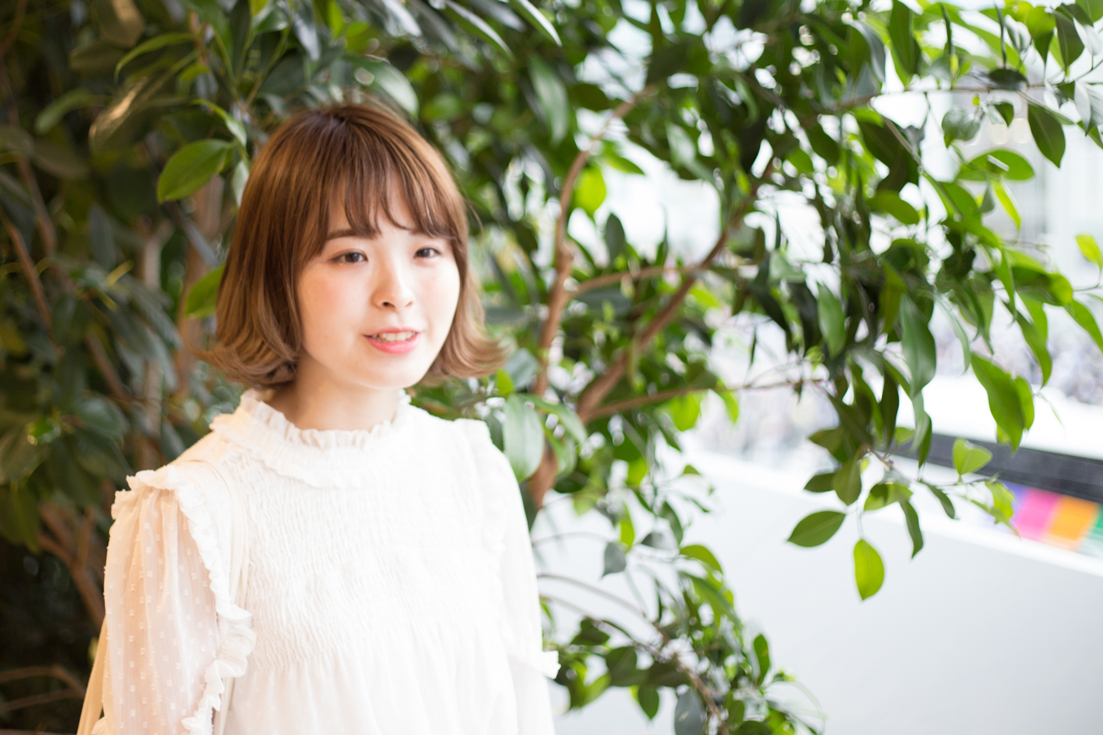 Portrait of a woman standing in front of green plants wearing a ruffled white blouse