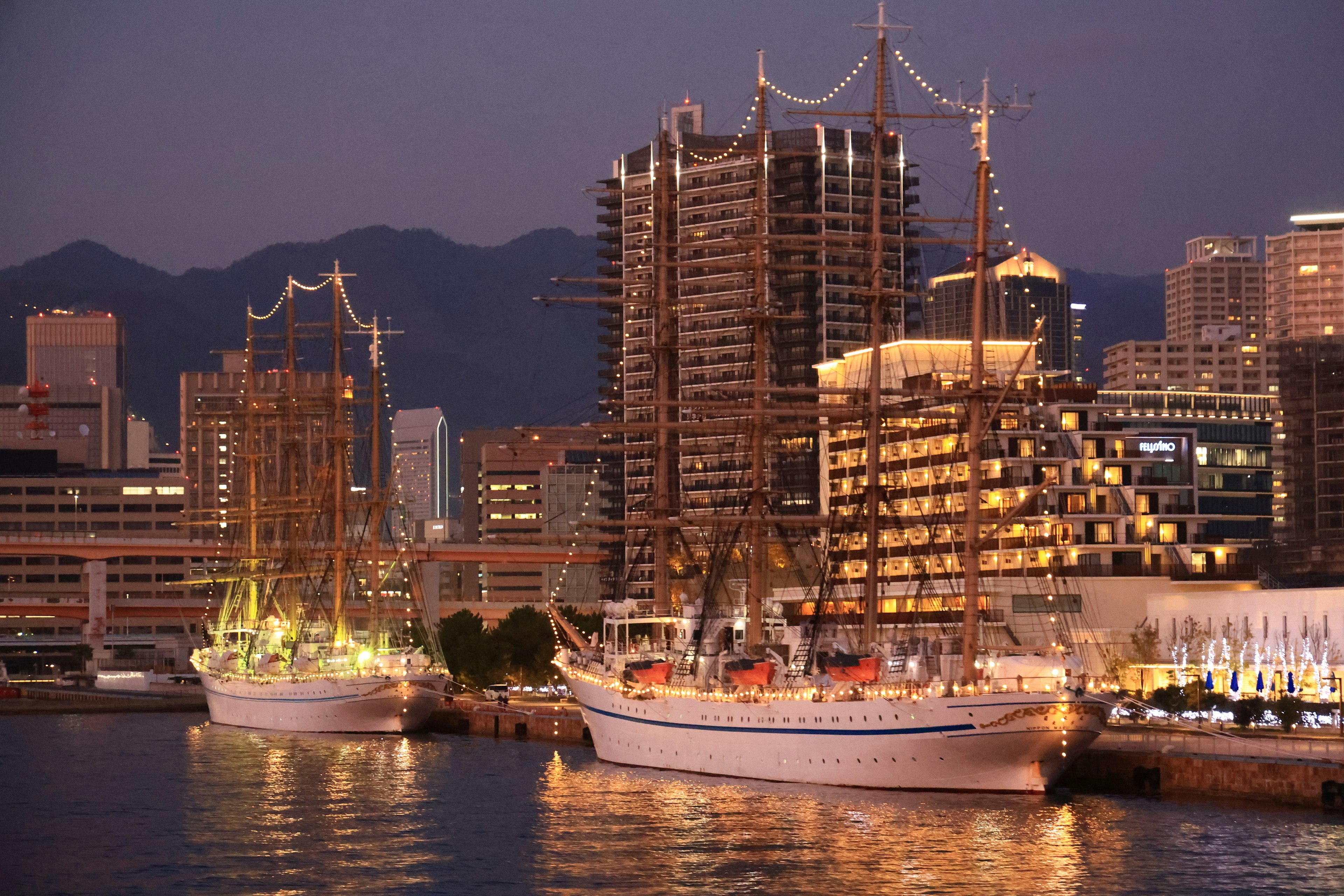 Beautiful sailing ships docked in a harbor at night with modern buildings