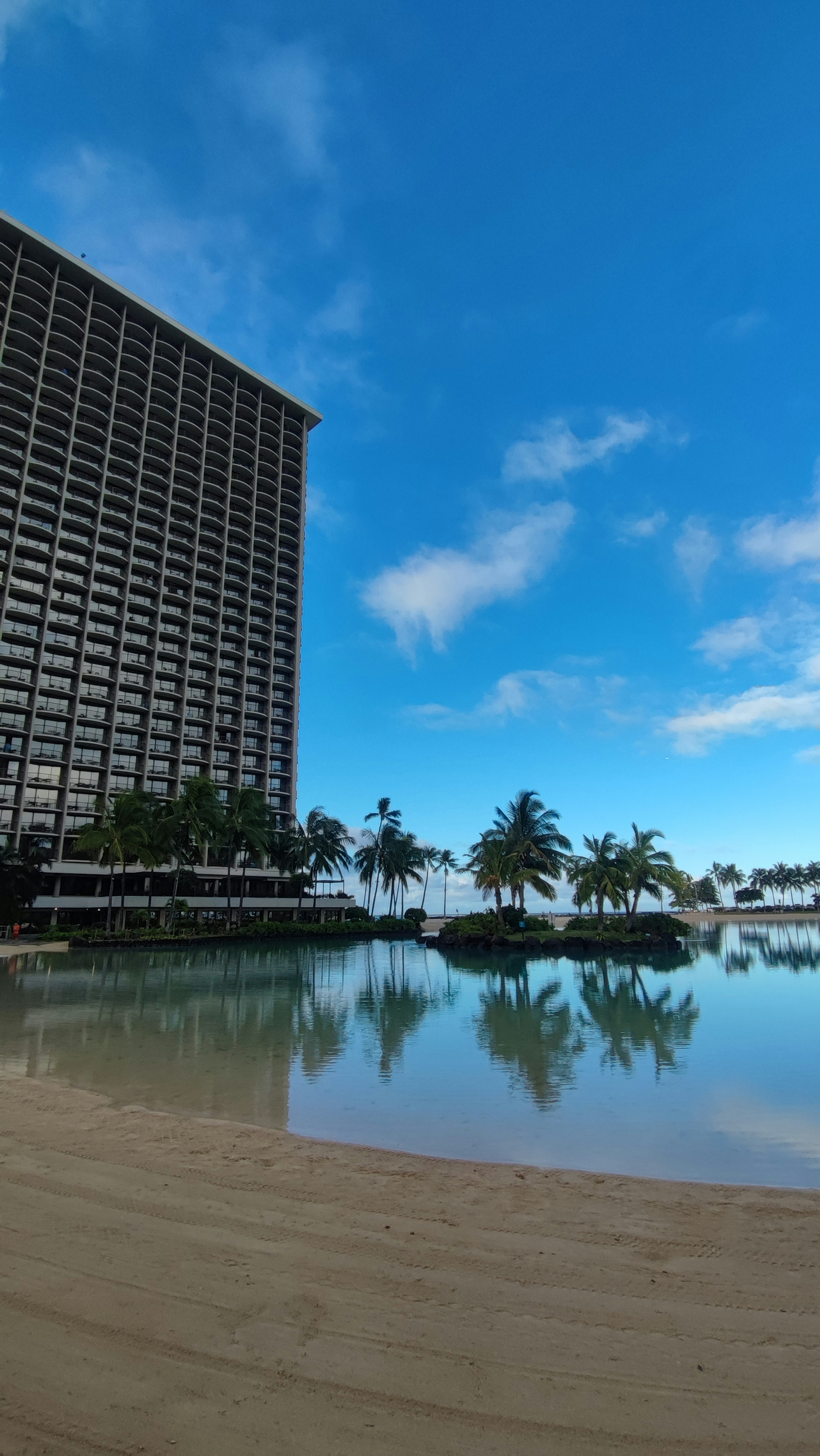 Pemandangan pantai dengan hotel resor yang terpantul di air dan langit biru yang cerah