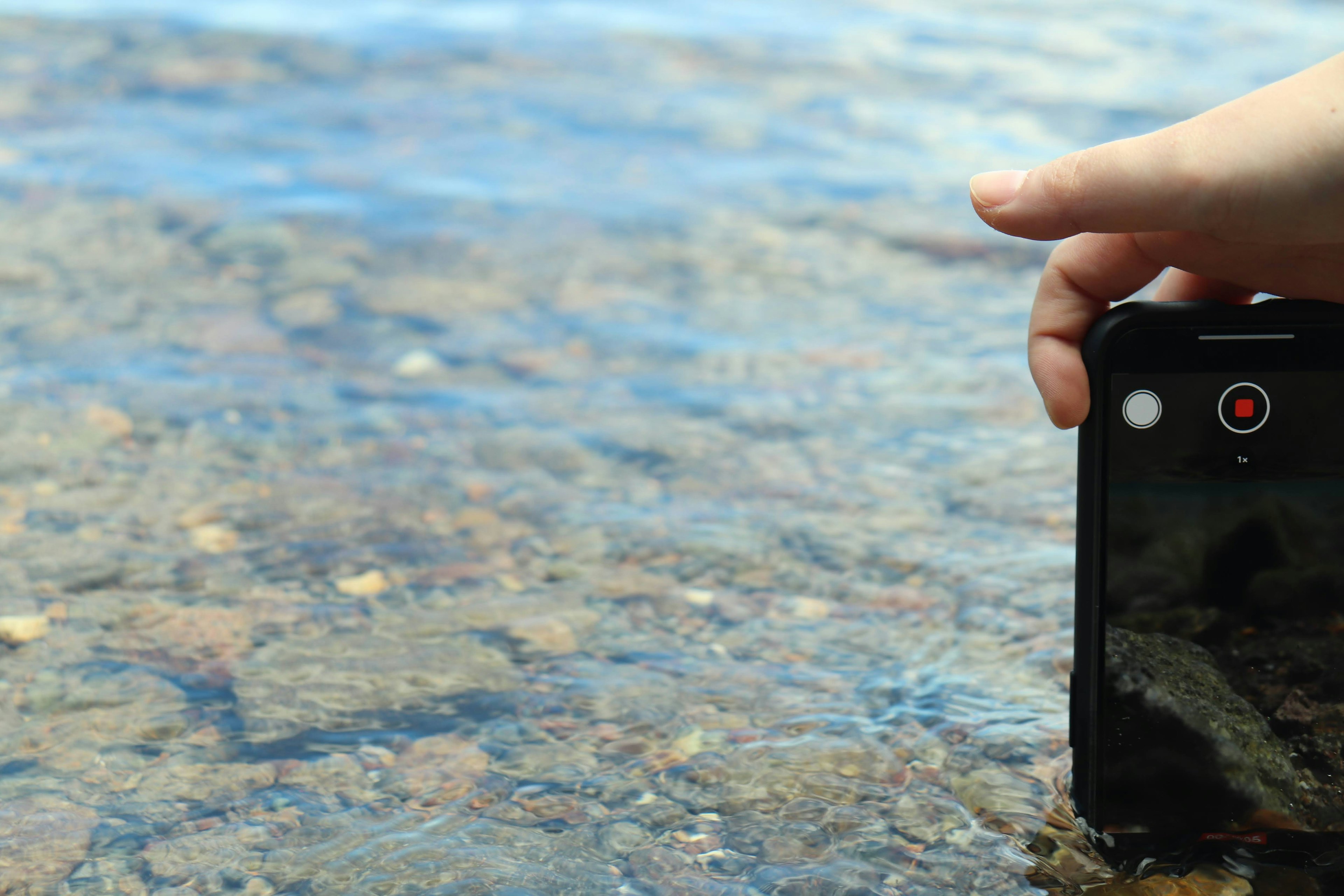 Hand holding a smartphone near a clear water surface