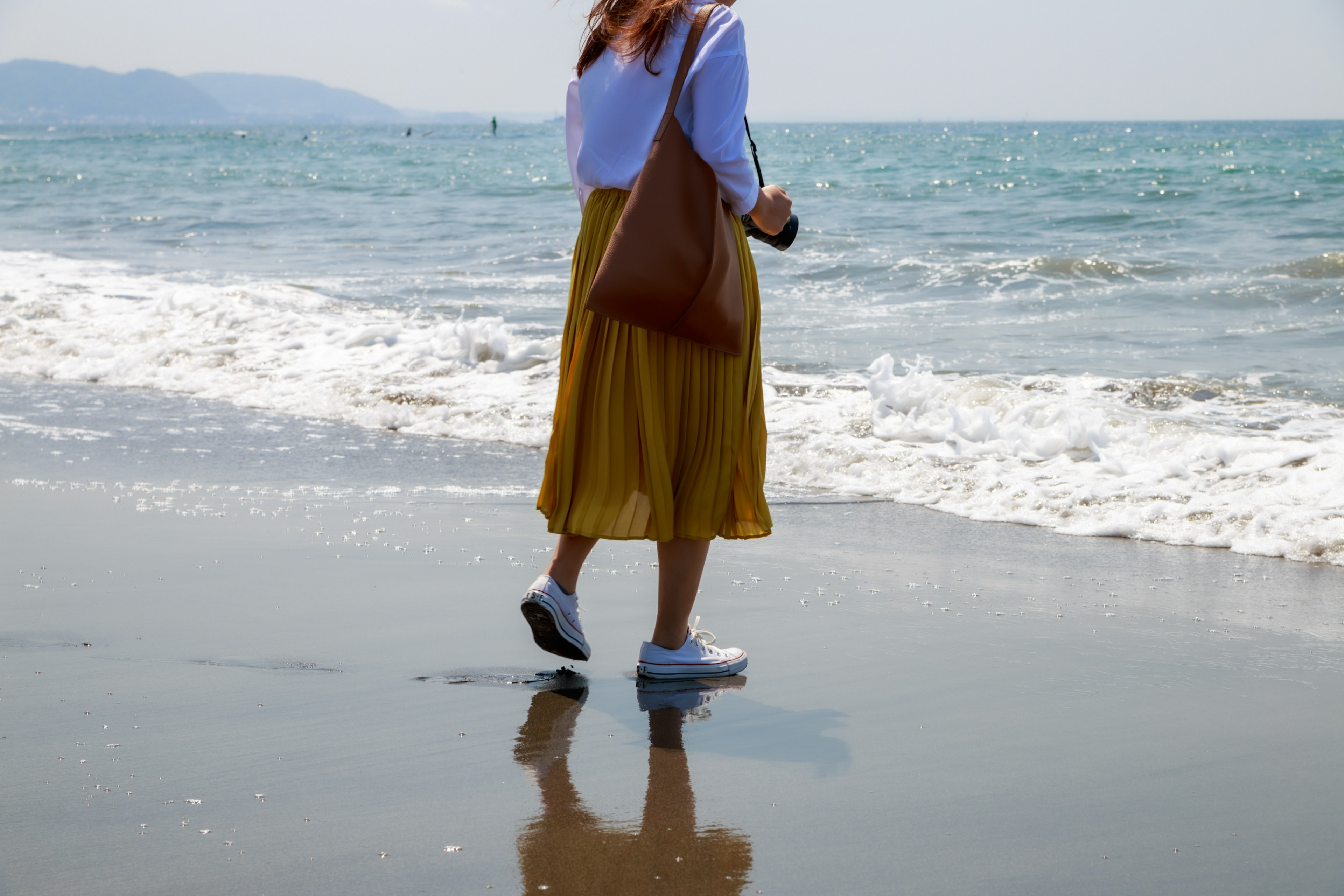 Mujer caminando por la playa con una camisa blanca y una falda amarilla