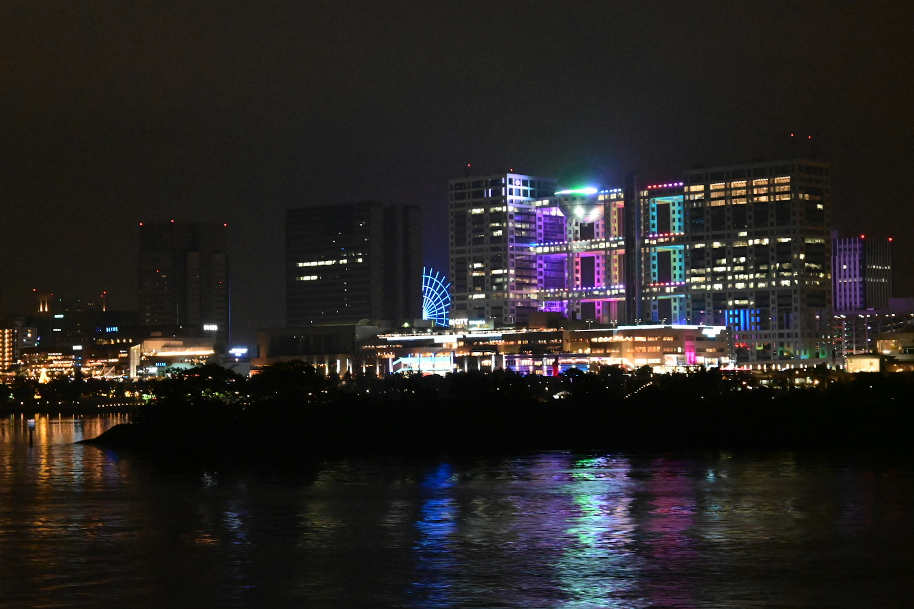 Bright city skyline at night with colorful lights reflecting on water