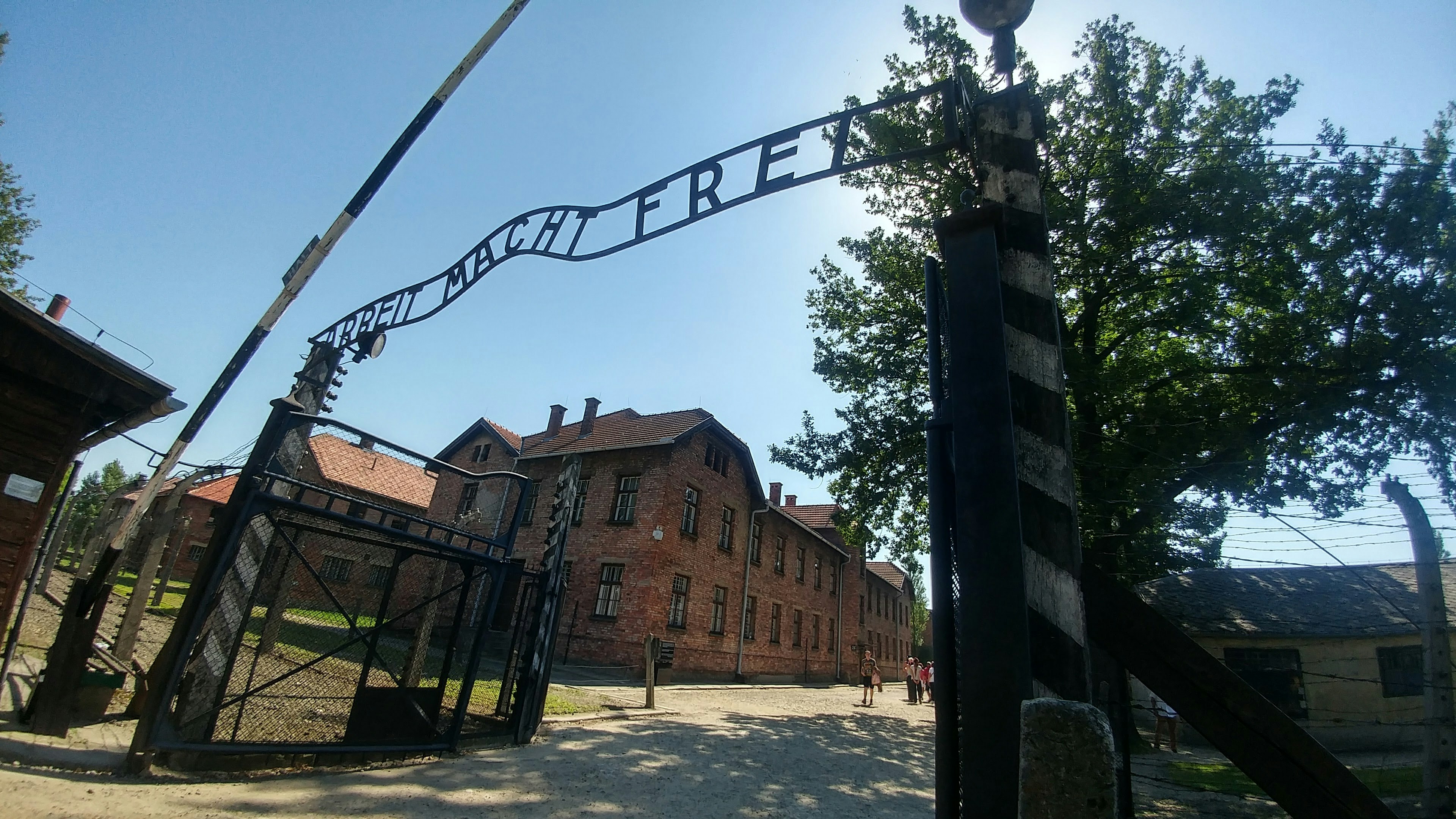 Cảnh cổng Auschwitz với một tòa nhà cũ và cánh cổng dưới bầu trời xanh