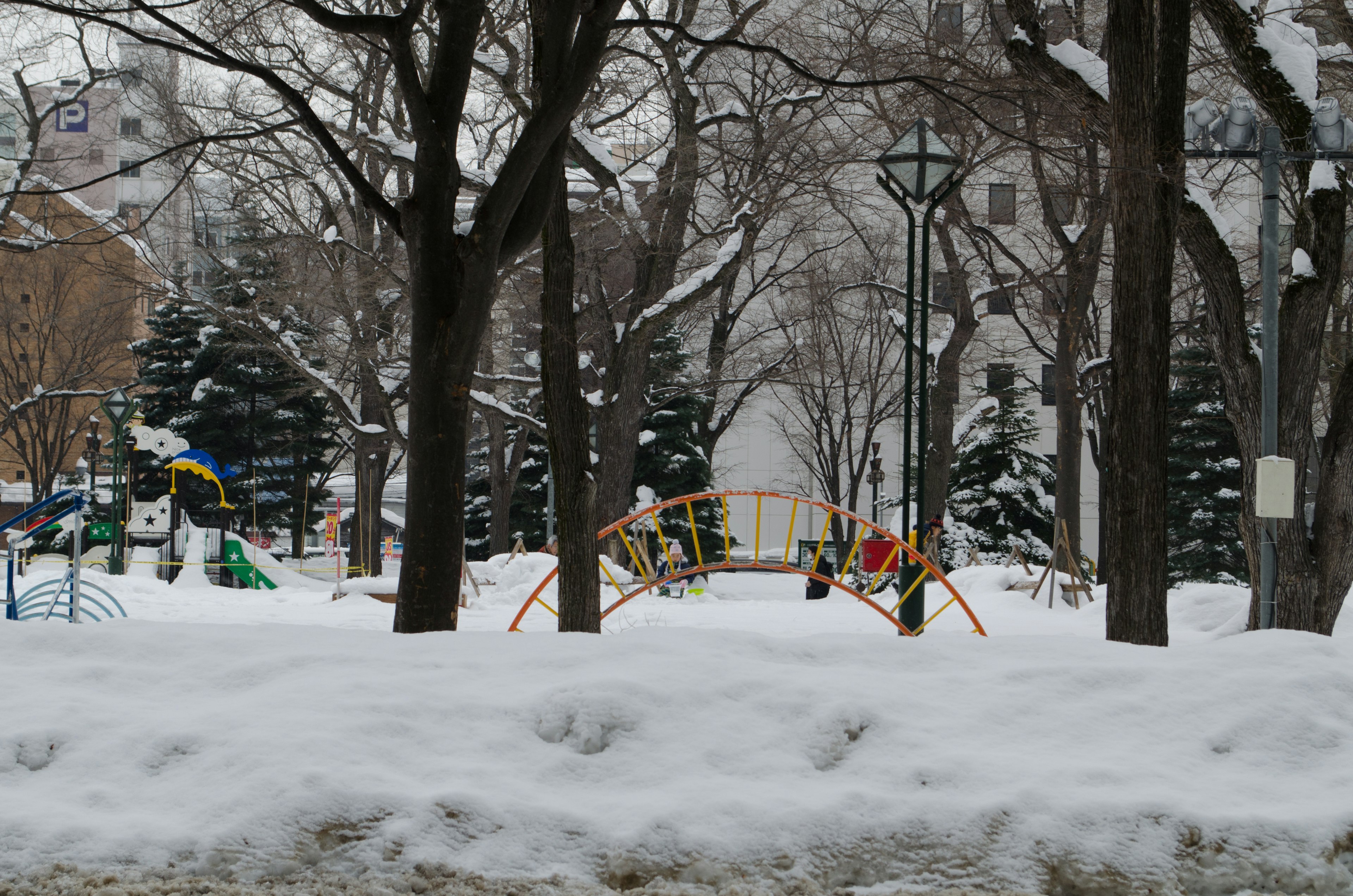 Parco giochi coperto di neve con attrezzature colorate e alberi spogli